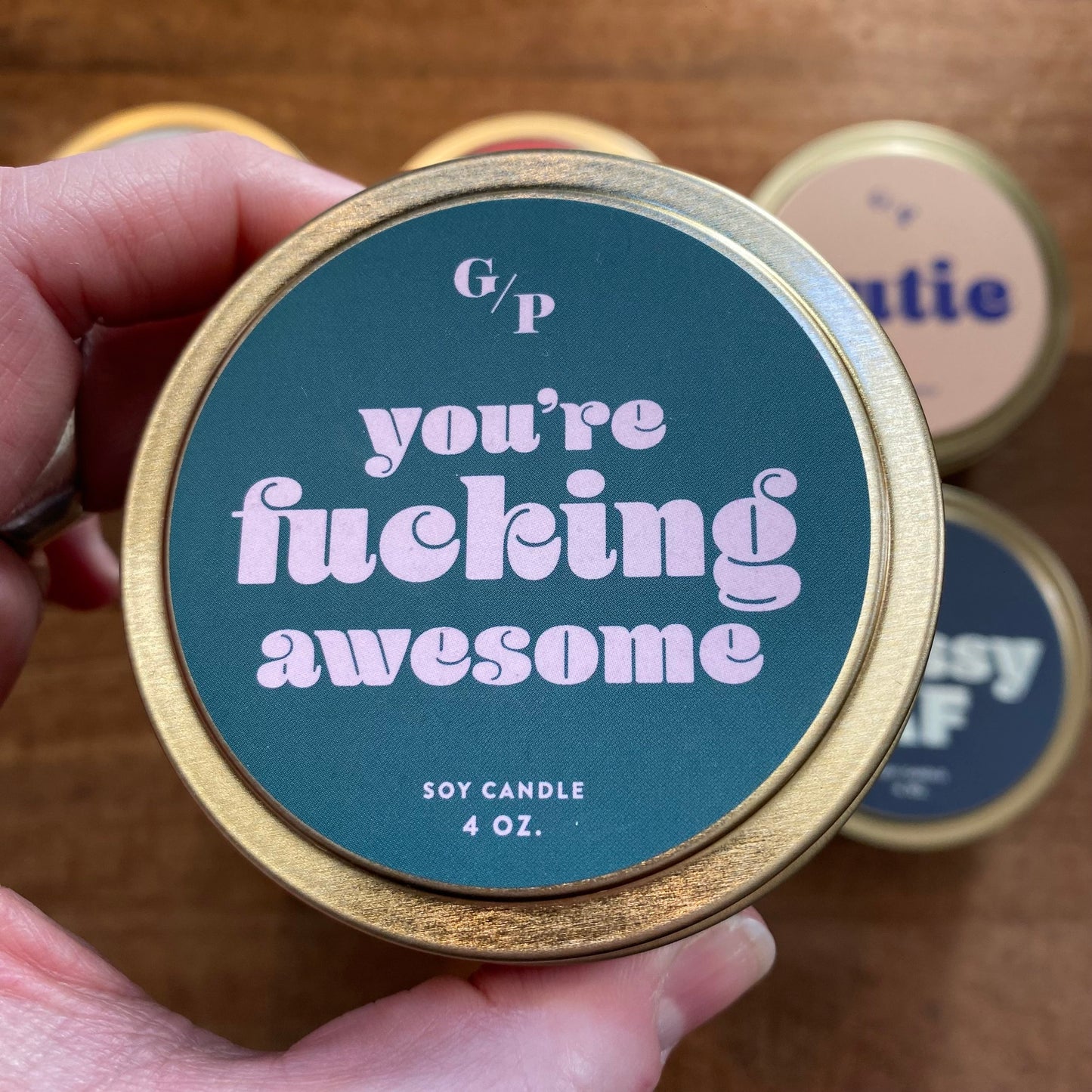 A hand holding a 4 oz. Tin Collection Soy Candle II by GP Candle Co with an encouraging message on the label.