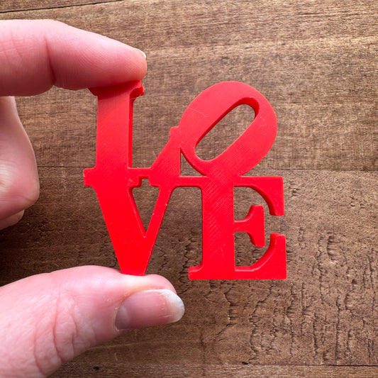 A hand holding a red, plastic cutout of the word