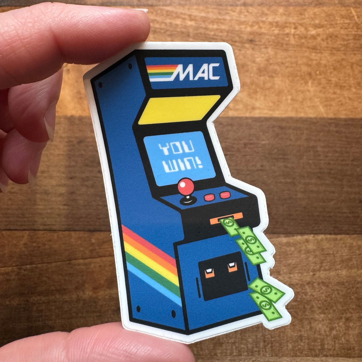 A hand holding a Philly Stickers II vinyl sticker of a stylized arcade machine with the text "you win" and money coming out the slot by South Fellini.