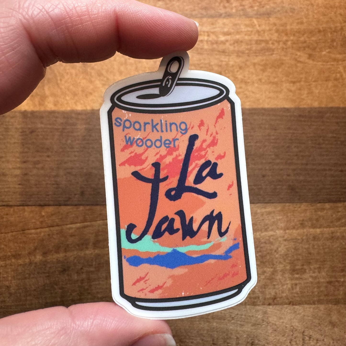 A hand holding a Philly Stickers II designed to resemble a soda can with the words "sparkling wooder - la jawn" written on it by South Fellini.