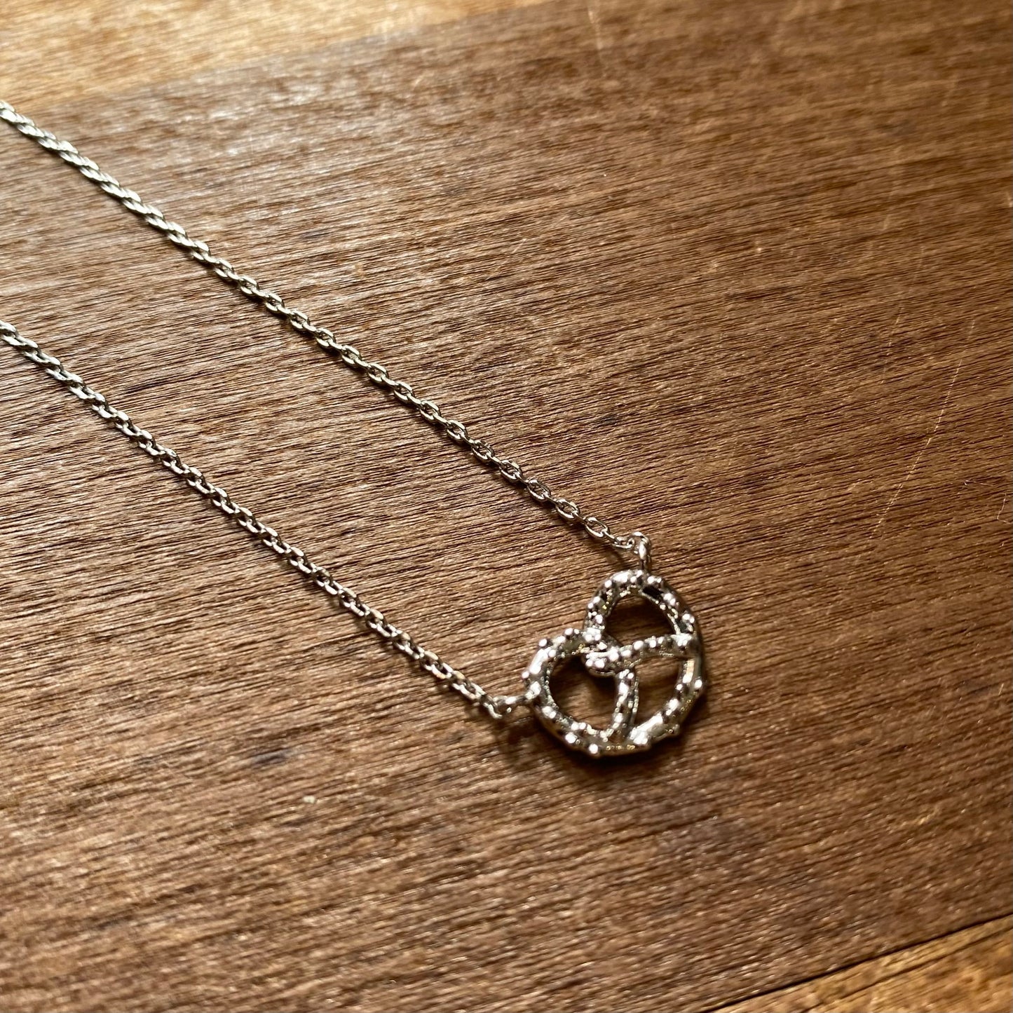 A LOVE & Pretzel Necklace with intertwined heart design from Lily Lough Jewelry on a wooden surface.