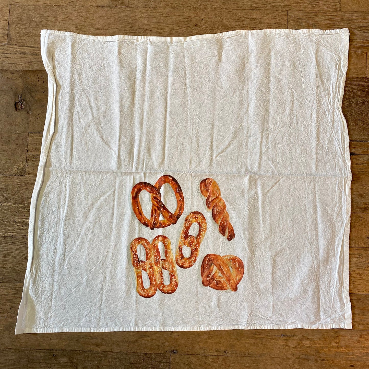 Soft pretzels arranged on a Meadowbrook Lane Philly Illustrated Tea Towel on a wooden surface.