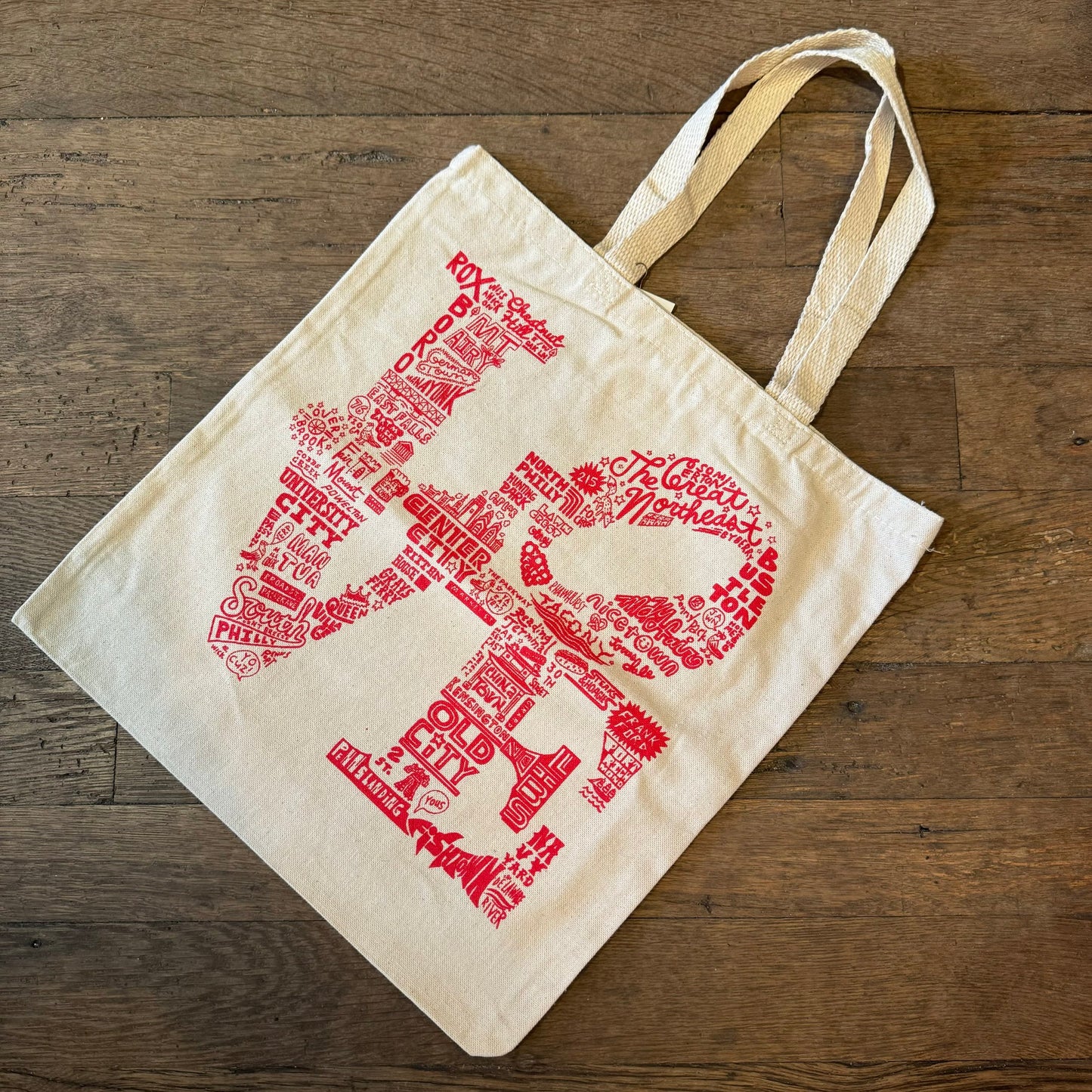 Canvas Paul Carpenter LOVE tote bag with red typographic design laid out on a wooden floor.