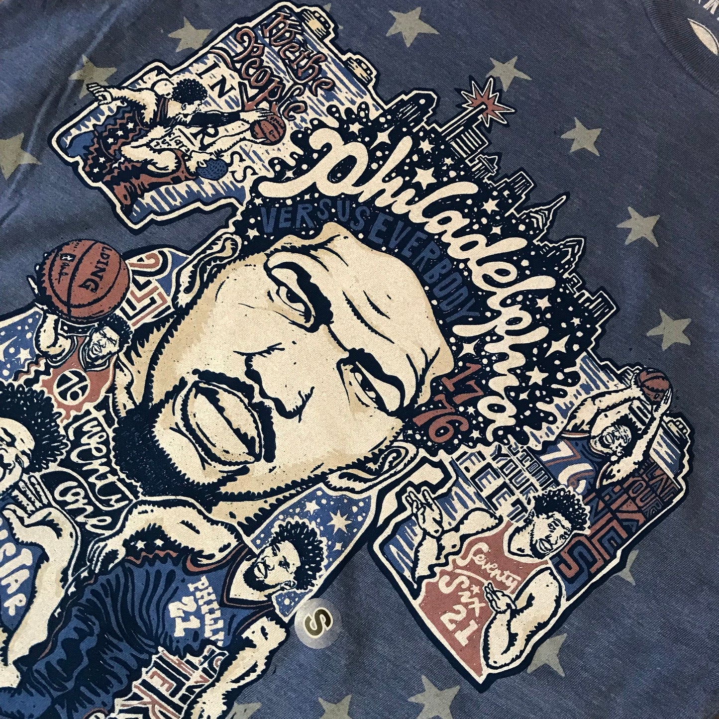 Graphic t-shirt featuring Sixers Joel Embiid T-Shirt with urban and basketball-themed illustrations and stylized text by Paul Carpenter.