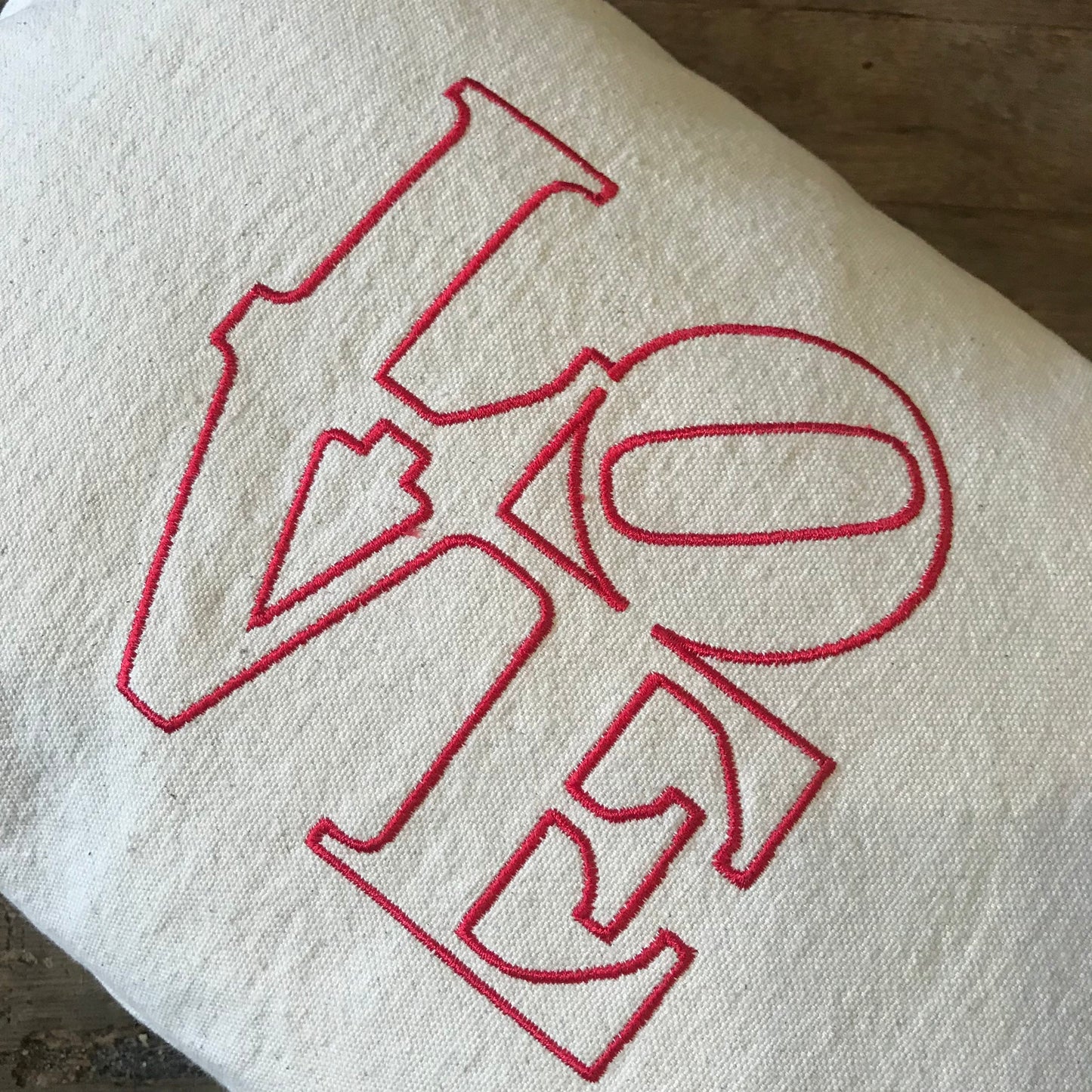 LOVE Embroidered Pillow by The Pillow Works, featuring an abstract design inspired by Robert Indiana's LOVE image, on white fabric.