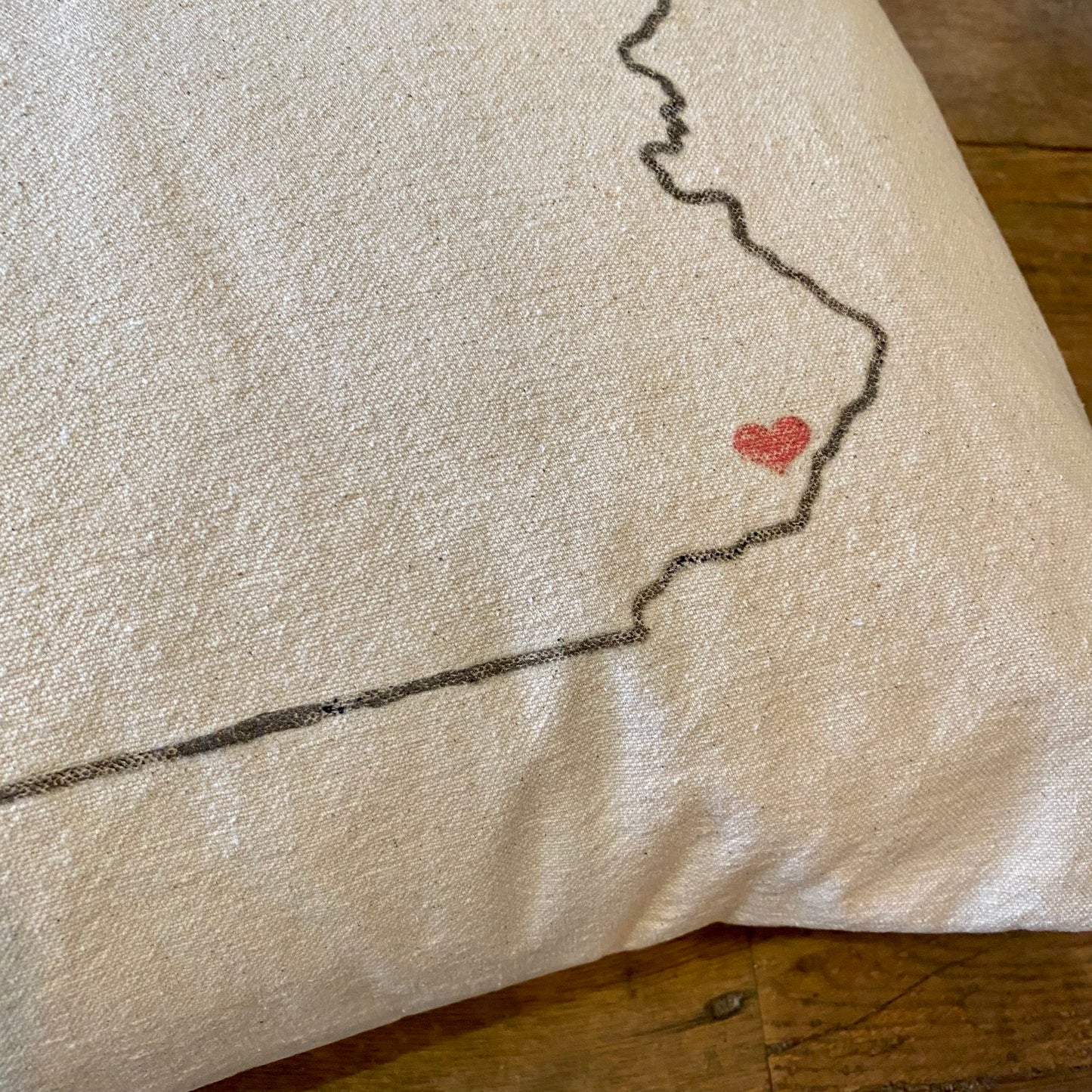 Close-up of The Pillow Works Pennsylvania Heart Pillow with a black stitched outline of a map and a small red heart embroidered on it.