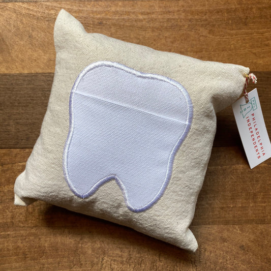 A Linen Appliqué Tooth Fairy Pillow by The Pillow Works with a tooth-shaped pocket on a wooden surface.