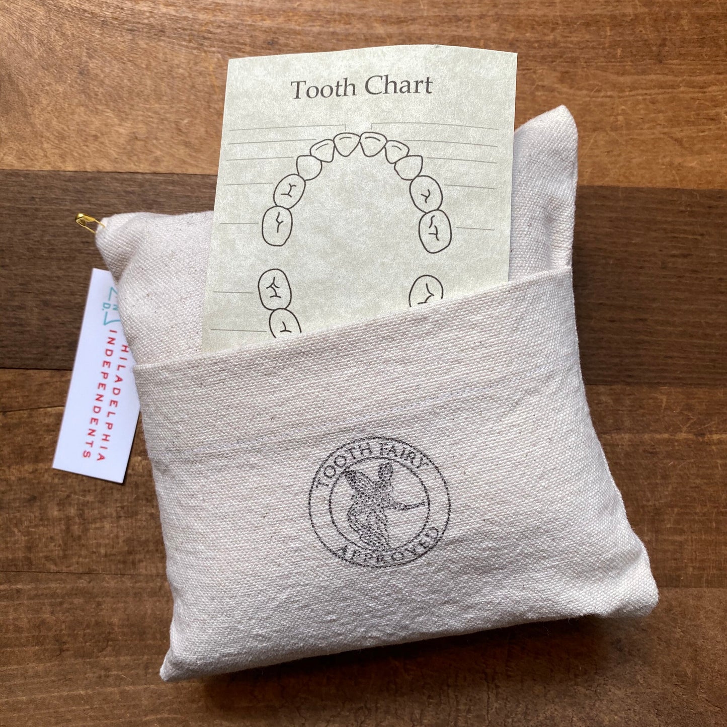 A tooth chart on top of a small appliqué The Pillow Works tooth fairy pillow on a wooden surface.