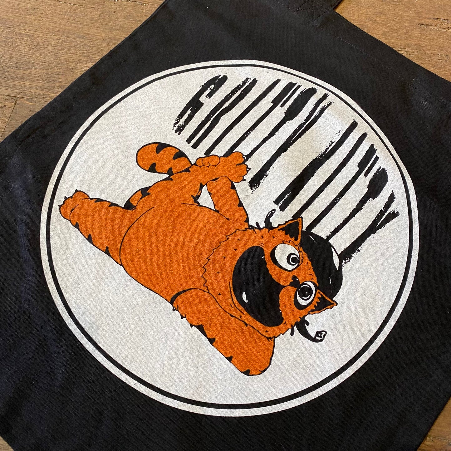 A Gritty Kitty Tote Bag featuring an illustration of an orange cartoon cat playfully leaping with a black striped background, hand-screenprinted on organic cotton by Slapstik.