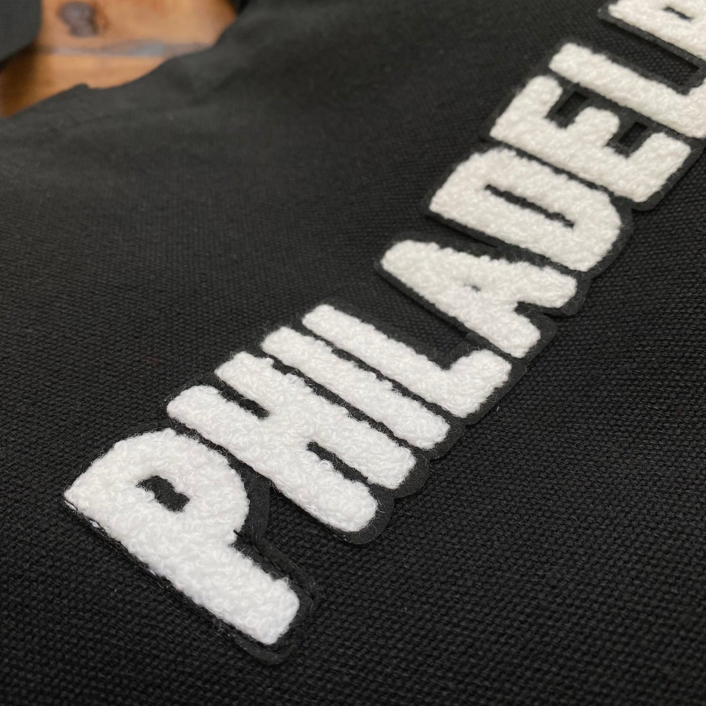Close-up of a black Tote Jawn Philadelphia Patch Tote Bag with the word "Philadelphia" embroidered in white, textured letters.