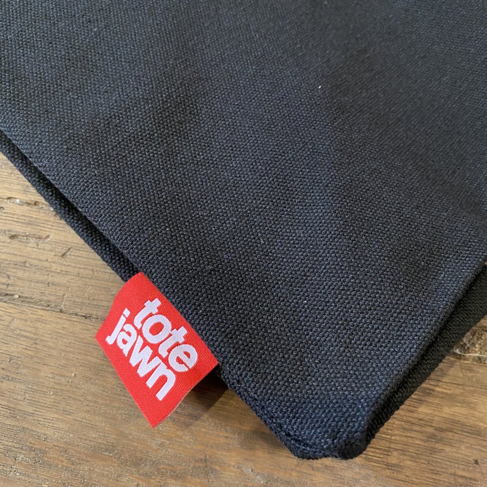 Close-up of a black Bell & Bolt Patch Tote Bag with a red and white "Tote Jawn" label.