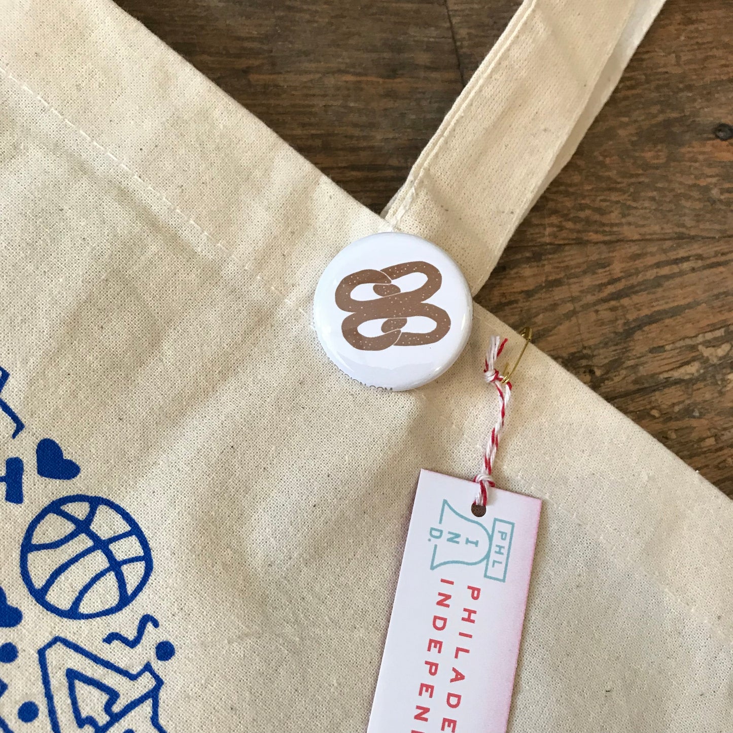 Close-up of a beige exit343design Philadelphia tote bag with a Liberty Bell pin and event tag attached.