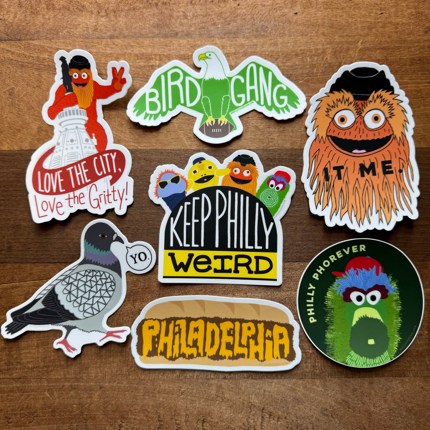 A set of colorful Philly Stickers from exit343design displayed on a wooden surface, showcasing lively phrases such as "Love the City, Love the Gritty," "BIRD GANG," "Philly Phorever," and "Keep Philly Weird.