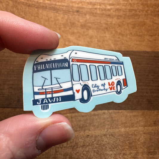 A person holding an Ana Thorne Philly Stickers III vinyl sticker shaped like a bus with Philadelphia-inspired illustrations and text.