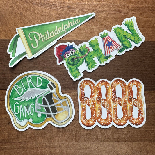 A set of four Philly-themed vinyl magnets from Meadowbrook Lane, featuring a Philadelphia Pennant, the Phillies mascot, an Eagles football helmet, and a pattern of pretzels spelling "LOVE", displayed on a wooden surface.