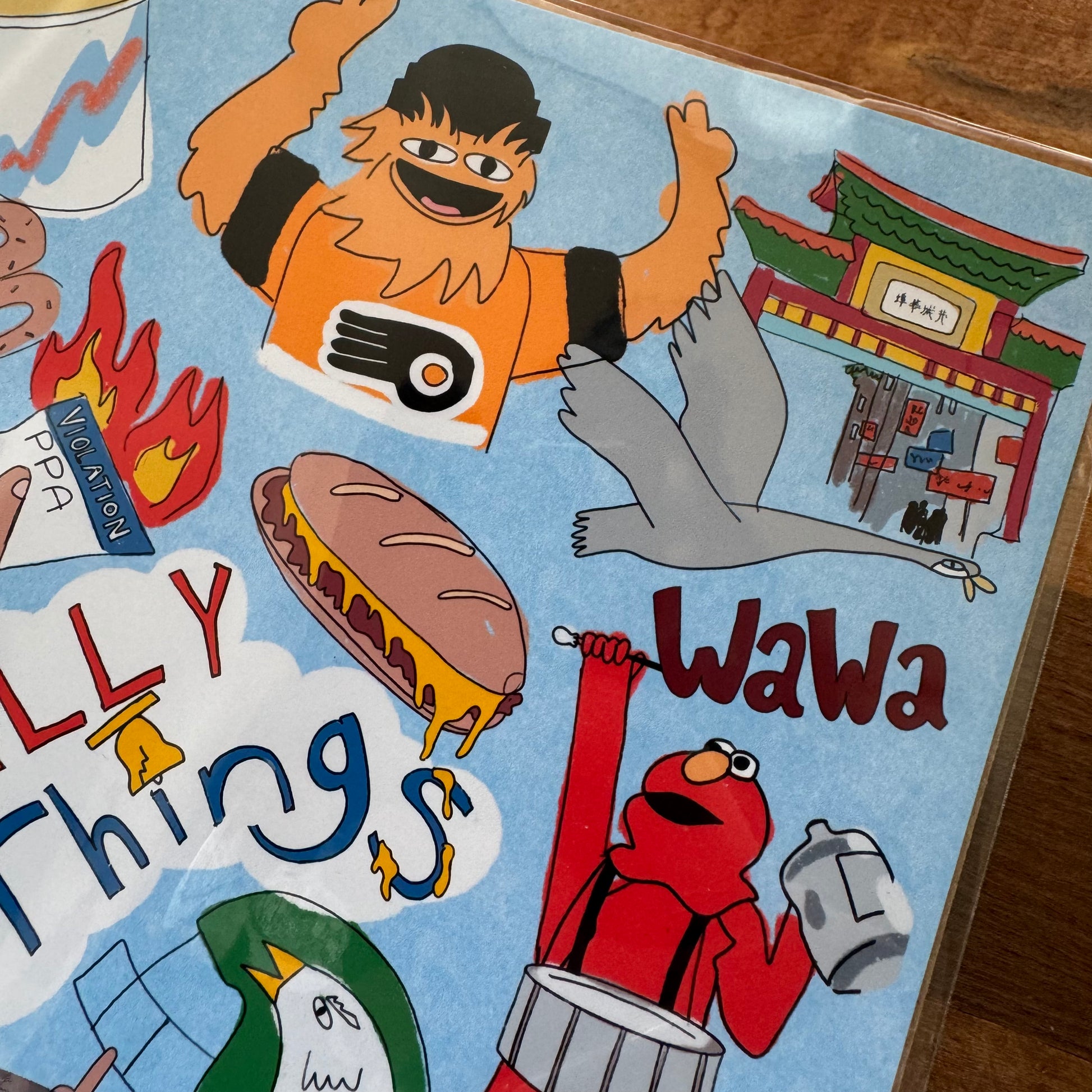 A colorful illustration by LizPopArt, titled "Philly Things Print," showcases an assortment of characters, such as a mascot in orange, a bird enjoying a sandwich, and a red character playing the drum. The text includes "WaWa" and "Silly Things," set against the backdrop of a pagoda. This print is available on professional matte premium paper.