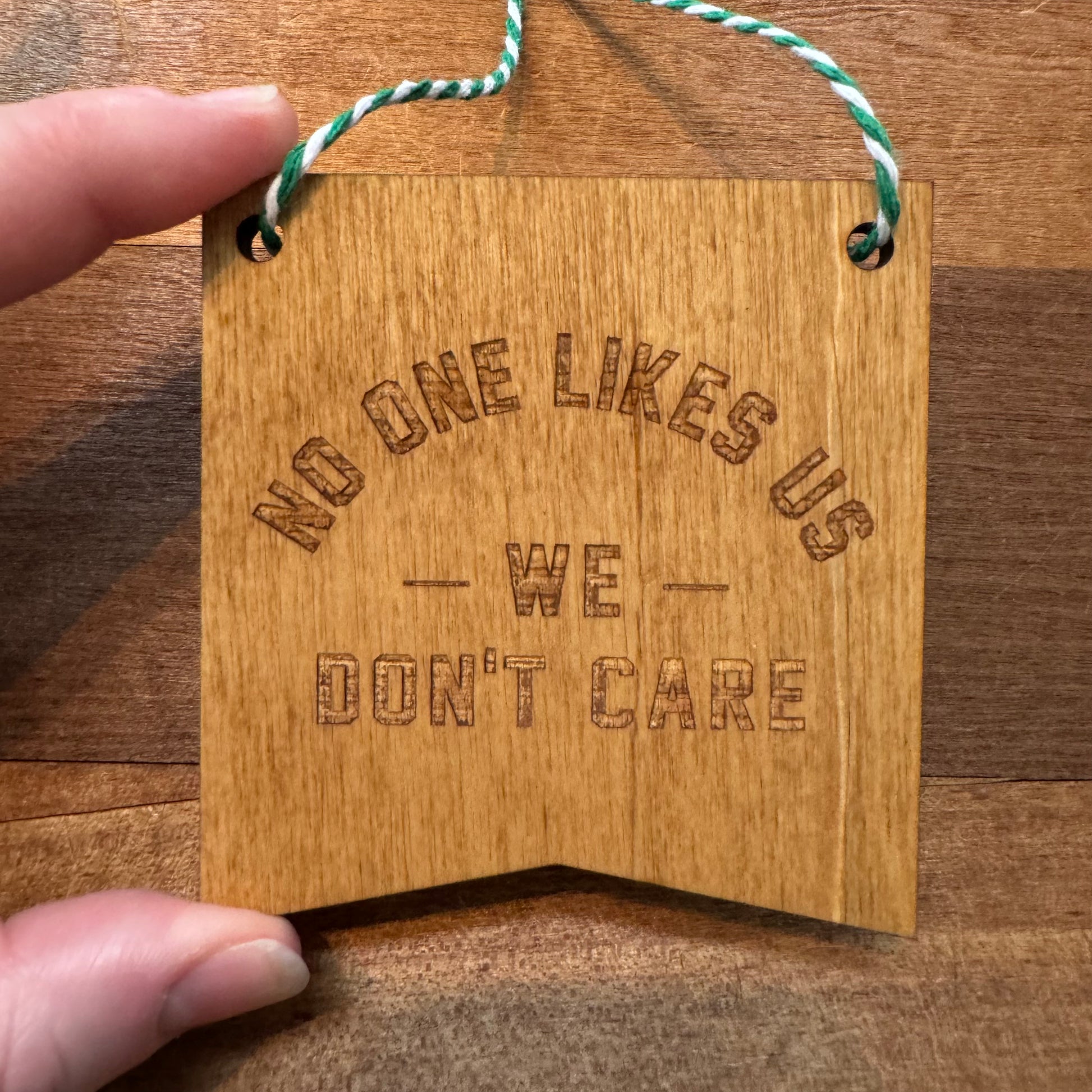 Frankadelphia's Philly Wood Ornaments featuring the text "NO ONE LIKES US - WE DON'T CARE" held by a hand against a wood background.