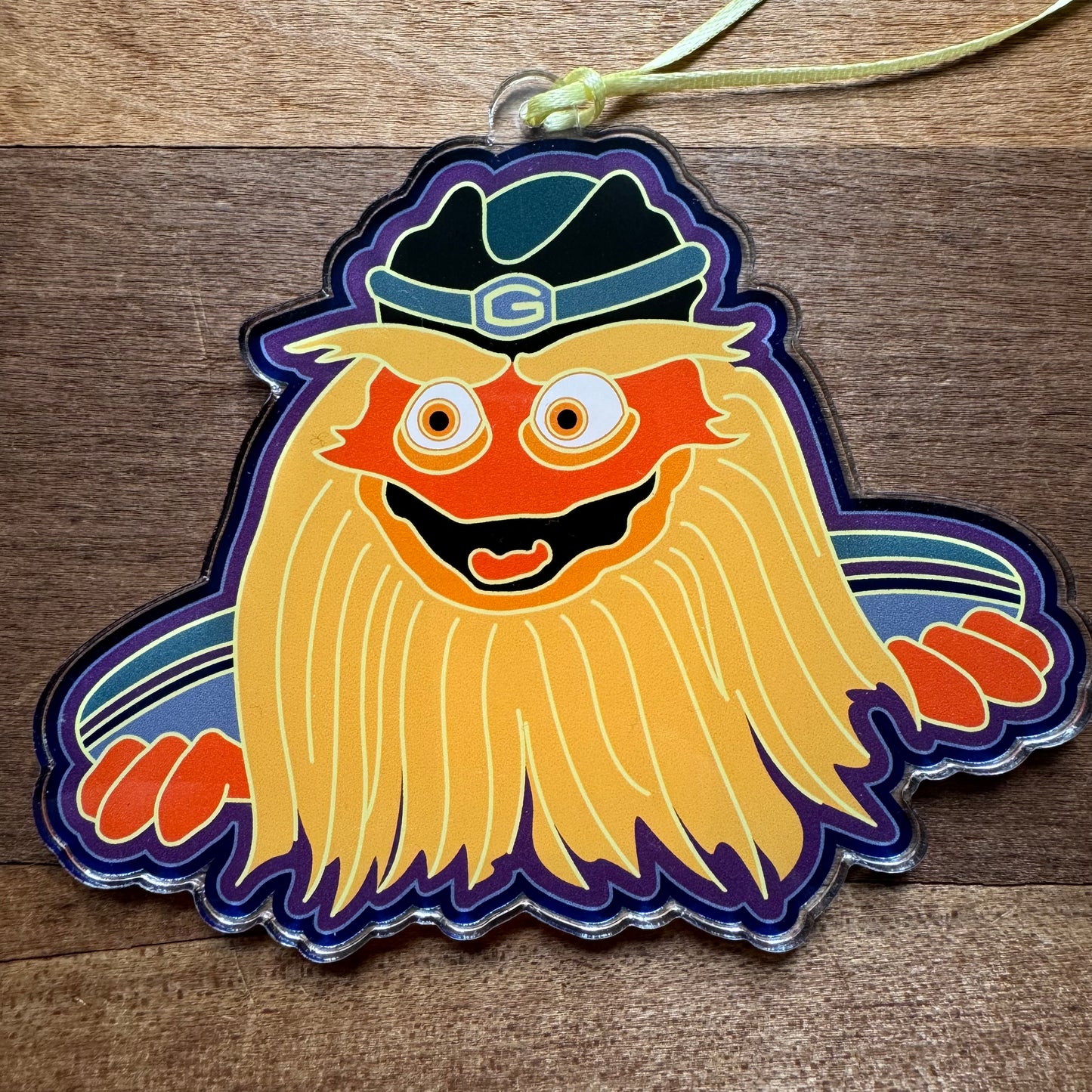 This acrylic ornament keychain, part of the "Philly Acrylic Ornaments III" collection by Jeffrey Arden Art, features a cartoon character with a big yellow beard and a green helmet, set against a wooden background.