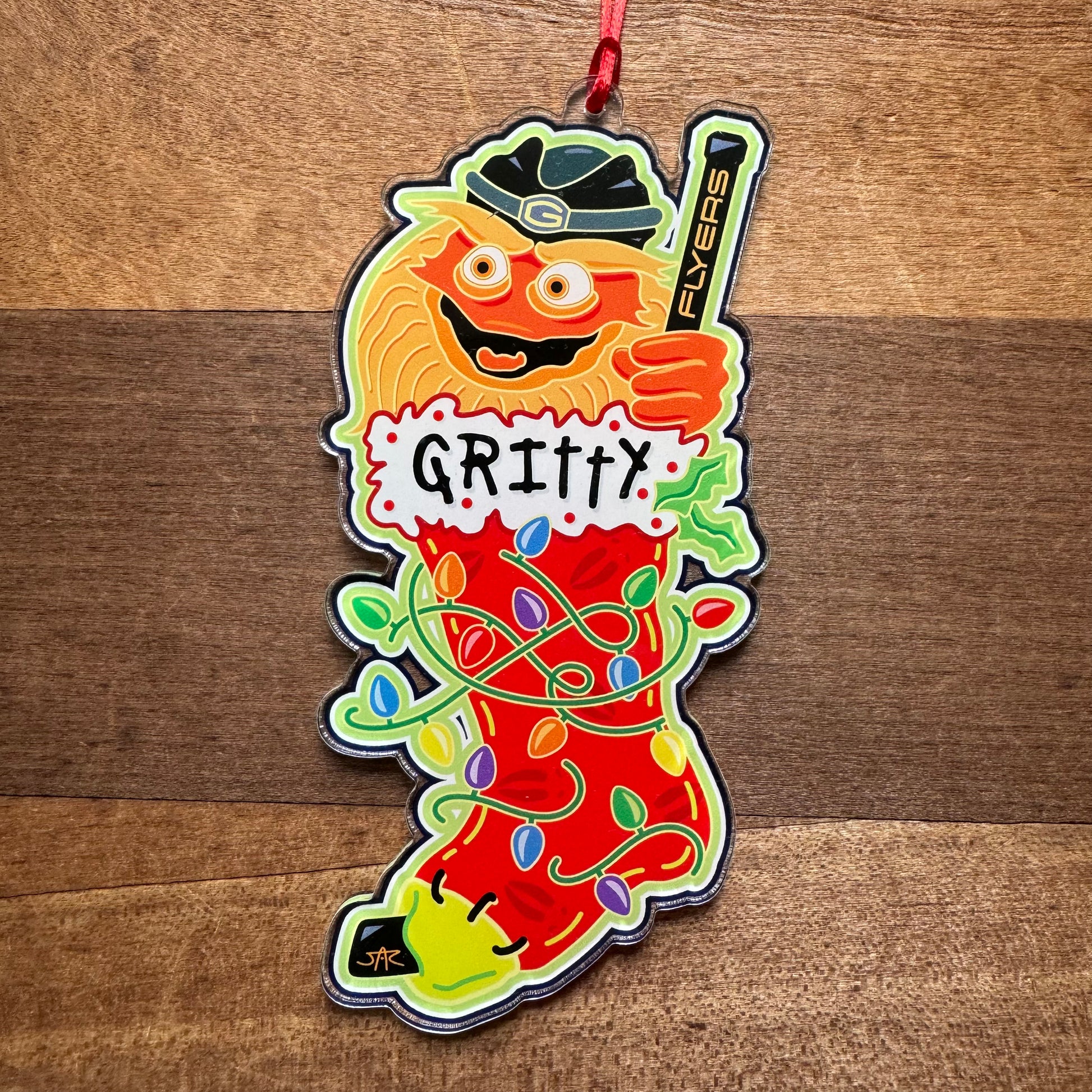 Celebrate the season with the 'Philly Acrylic Ornaments III' from Jeffrey Arden Art. This festive ornament showcases a Philly sports-themed design featuring a popular hockey mascot, "Gritty," on a Christmas stocking adorned with holiday lights and holding a hockey stick—perfect for any fan!