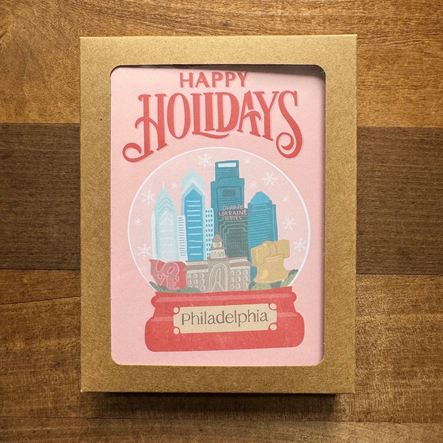 The Holiday Card Packs II from Parcel Island feature a charming snow globe illustration showcasing Philadelphia landmarks with "Happy Holidays" text, set against a wooden background. These Philly cards come complete with envelopes, making them perfect for sending festive cheer to friends and family.