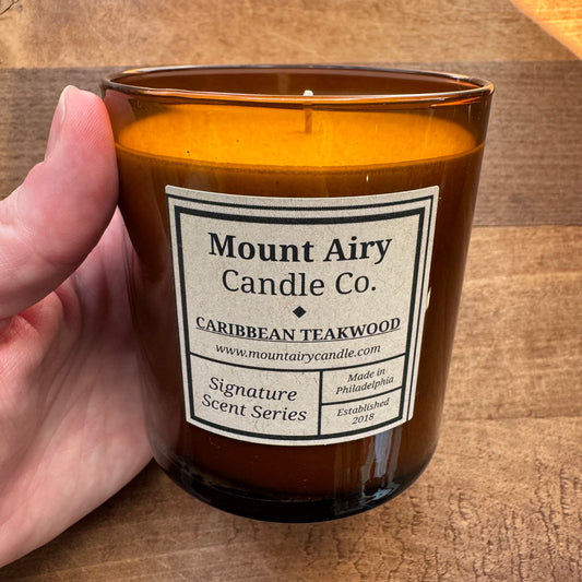 A hand holds a brown glass Soy Candle from Mount Airy Candle Co. The label reads 