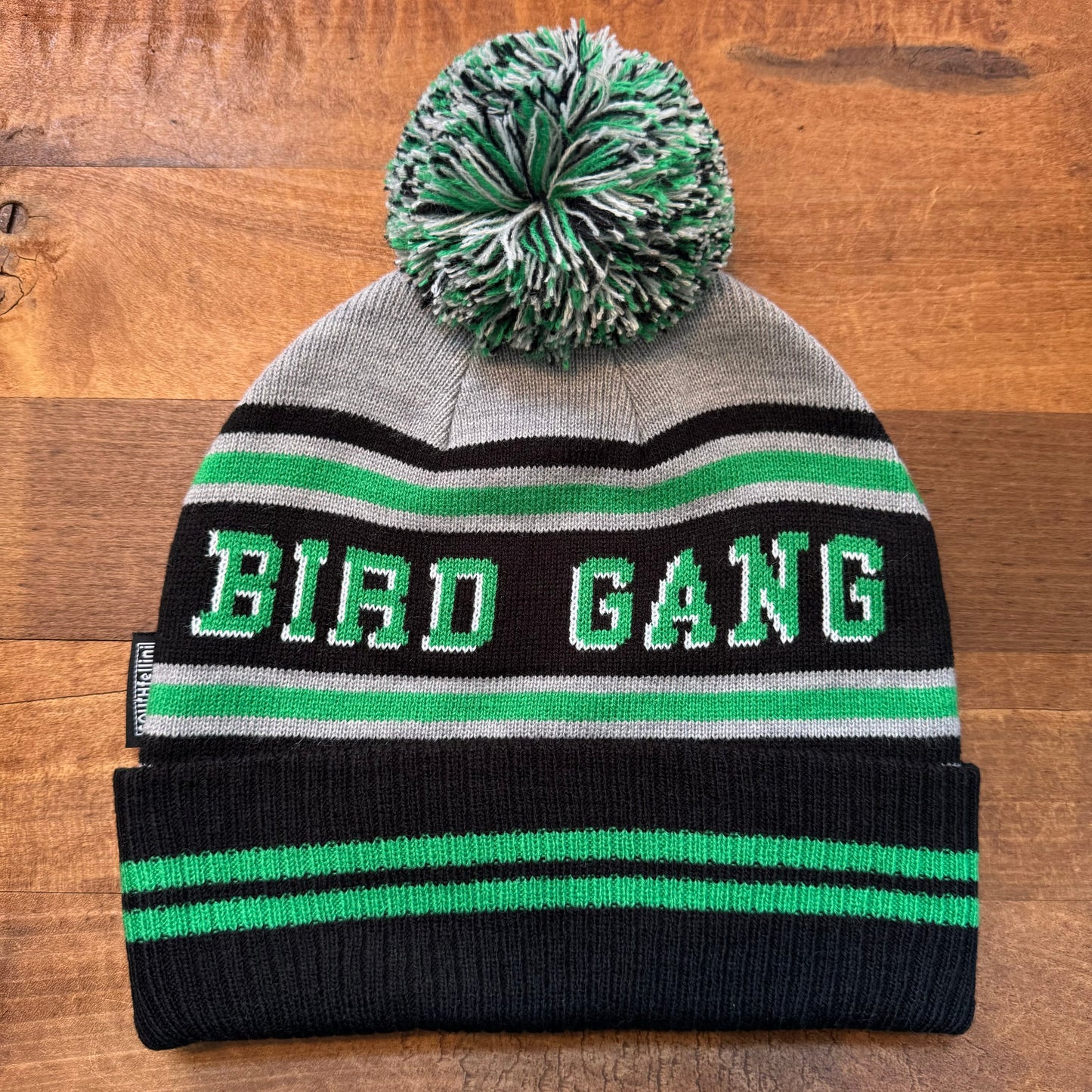 The Bird Gang Eagles Beanie from South Fellini is a double-sided knit hat with a pom-pom on top, featuring gray, black, and green stripes and the words "BIRD GANG" embroidered in white text—perfect for any Eagles fan.