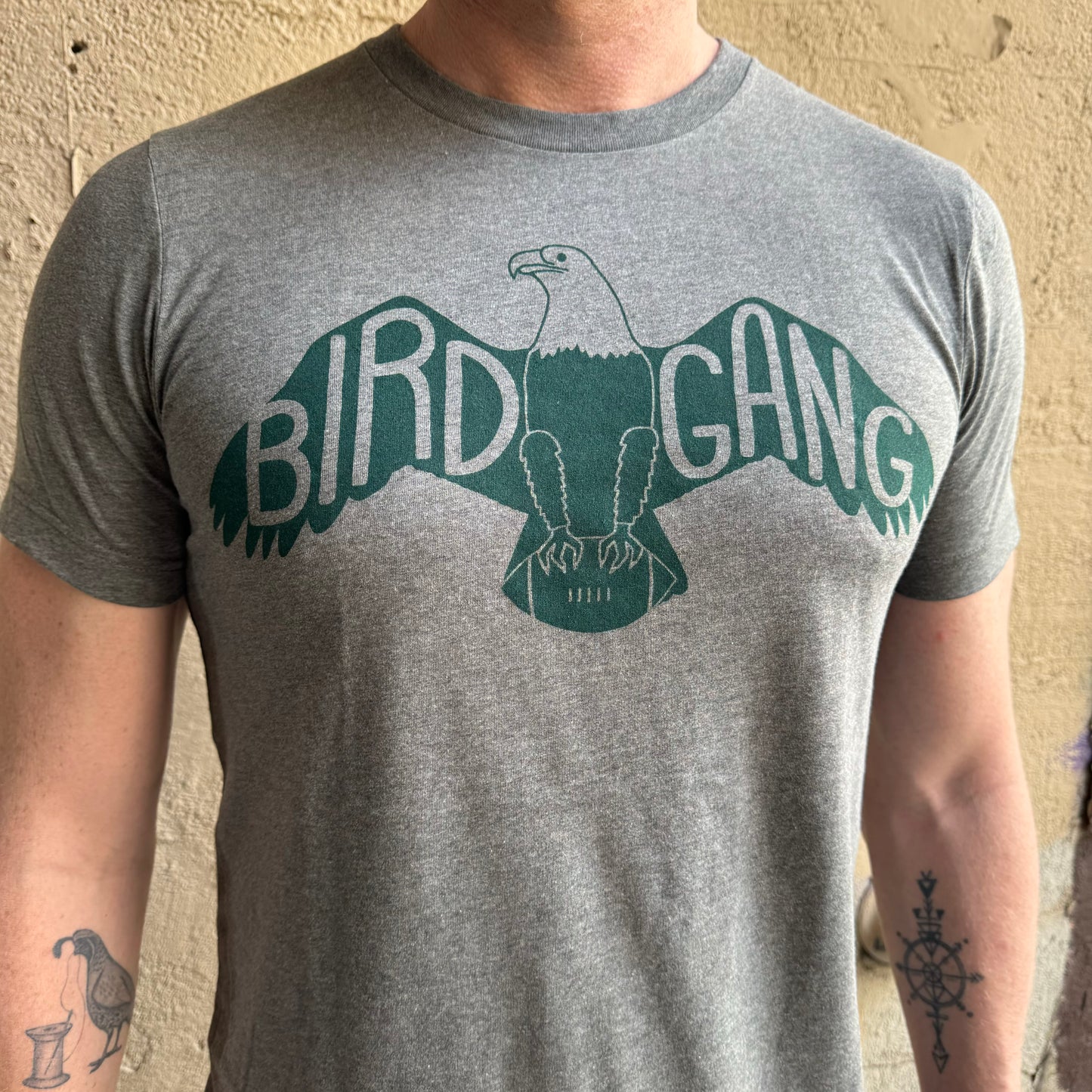 A person wearing a unisex exit343design Bird Gang T-Shirt featuring an illustration of an eagle with the words "Philly’s Bird Gang" on its wings.