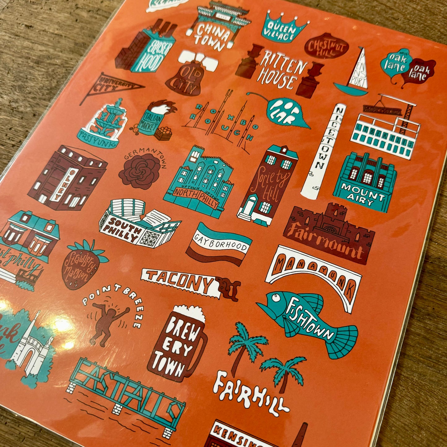 The Philadelphia Prints by Kate Otte feature an illustrated map on an orange background that showcases Philly neighborhoods with small drawings and names such as Chinatown, Rittenhouse, Fishtown, and Brewerytown. This charming piece captures the essence of Philly Lingo and makes a perfect addition to any collection of Philly-themed prints.