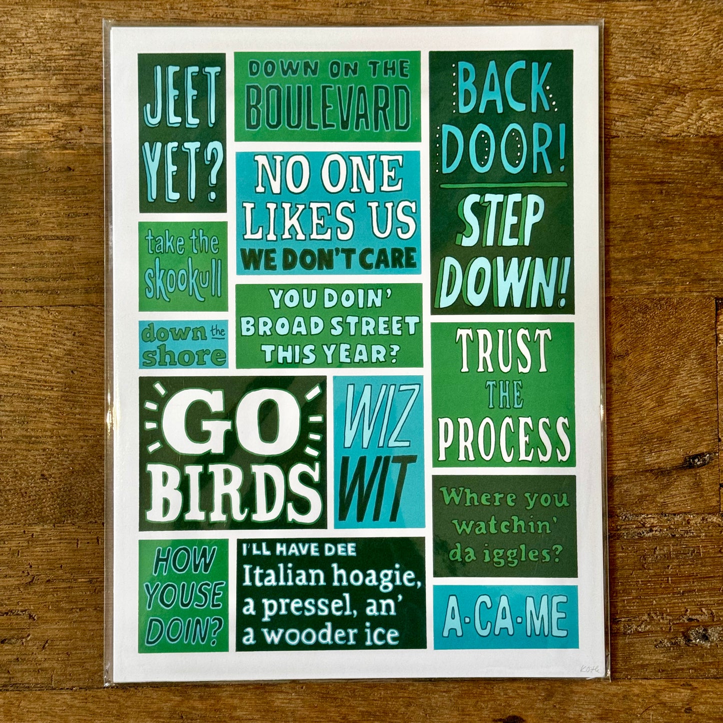 Introducing Philadelphia Prints by Kate Otte – this poster features an array of Philly-themed phrases like "Jeet Yet?", "GO BIRDS," "WIZ WIT," "STEP DOWN," and "TRUST THE PROCESS" in diverse fonts and colors, all set against a wooden background. Ideal for anyone who loves authentic Philly lingo.