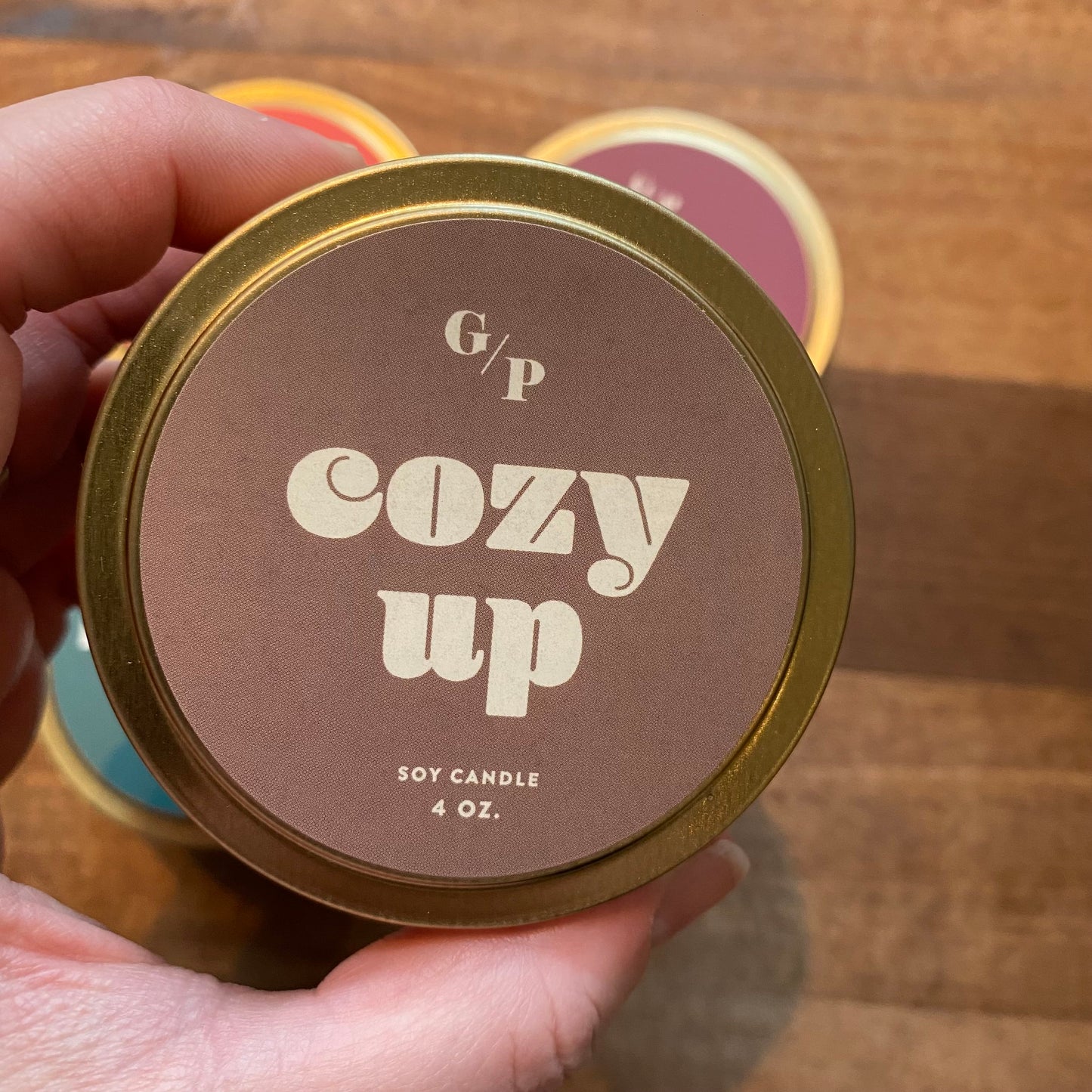 A hand holding a small Tin Collection Soy Candle II tin labeled "cozy up" by GP Candle Co.