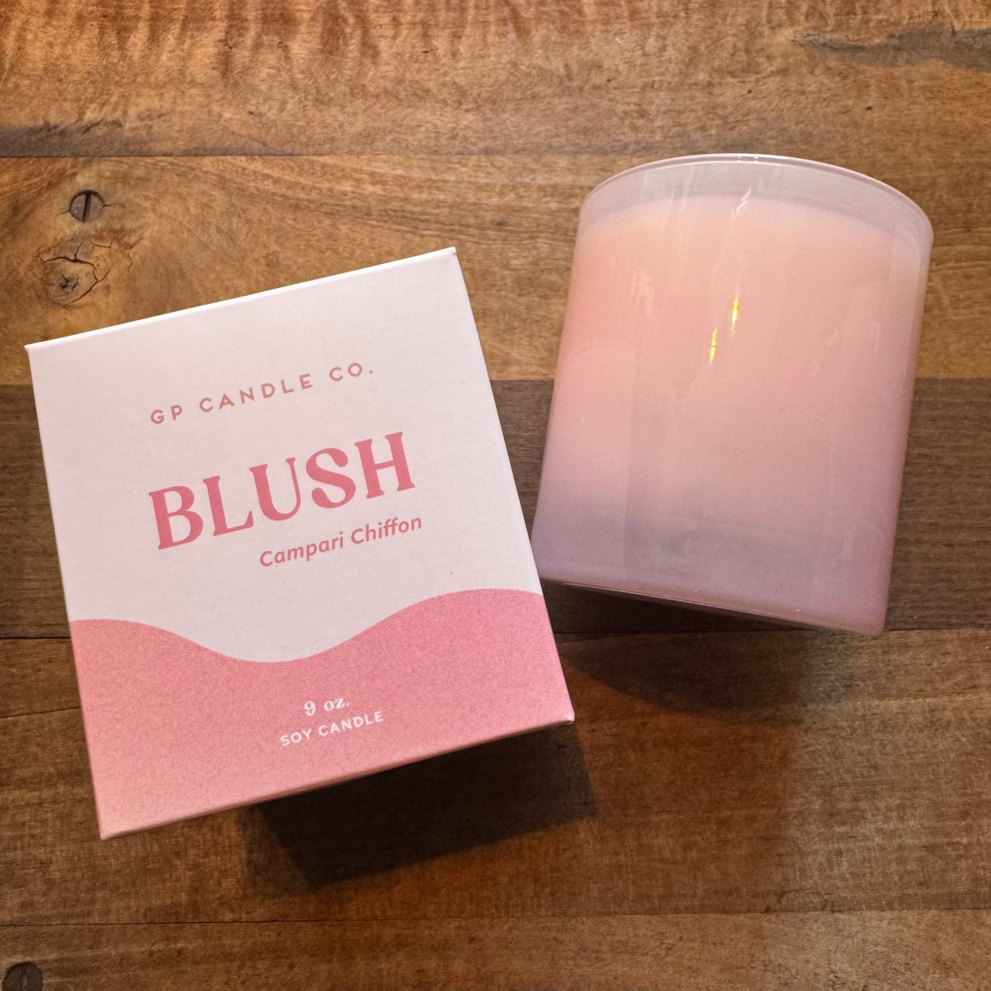 A blush-colored GP Candle Co Hue Collection soy candle beside its packaging on a wooden surface.