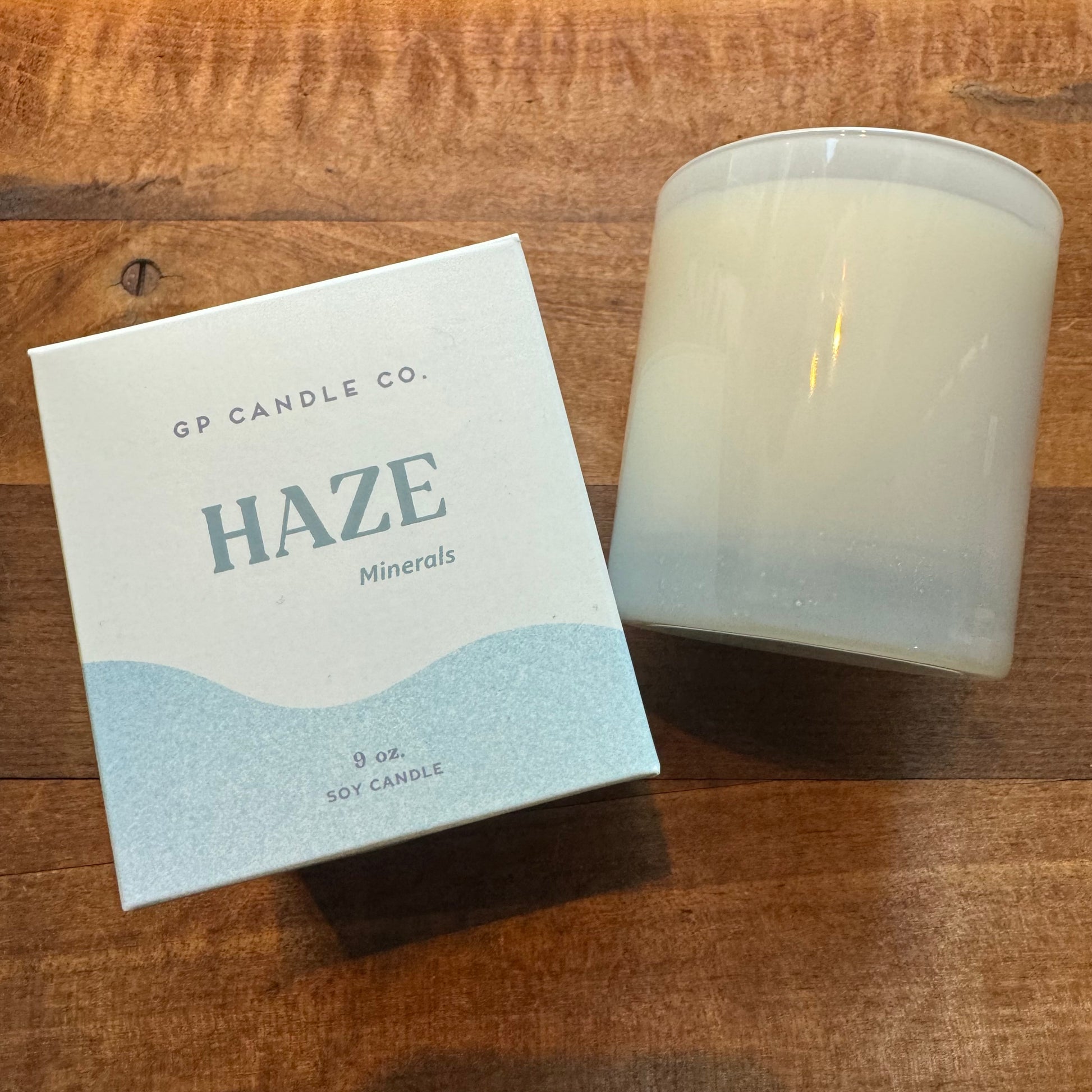 A hand-poured soy candle from GP Candle Co named "Soy Candles-Hue Collection" beside its packaging on a wooden surface.