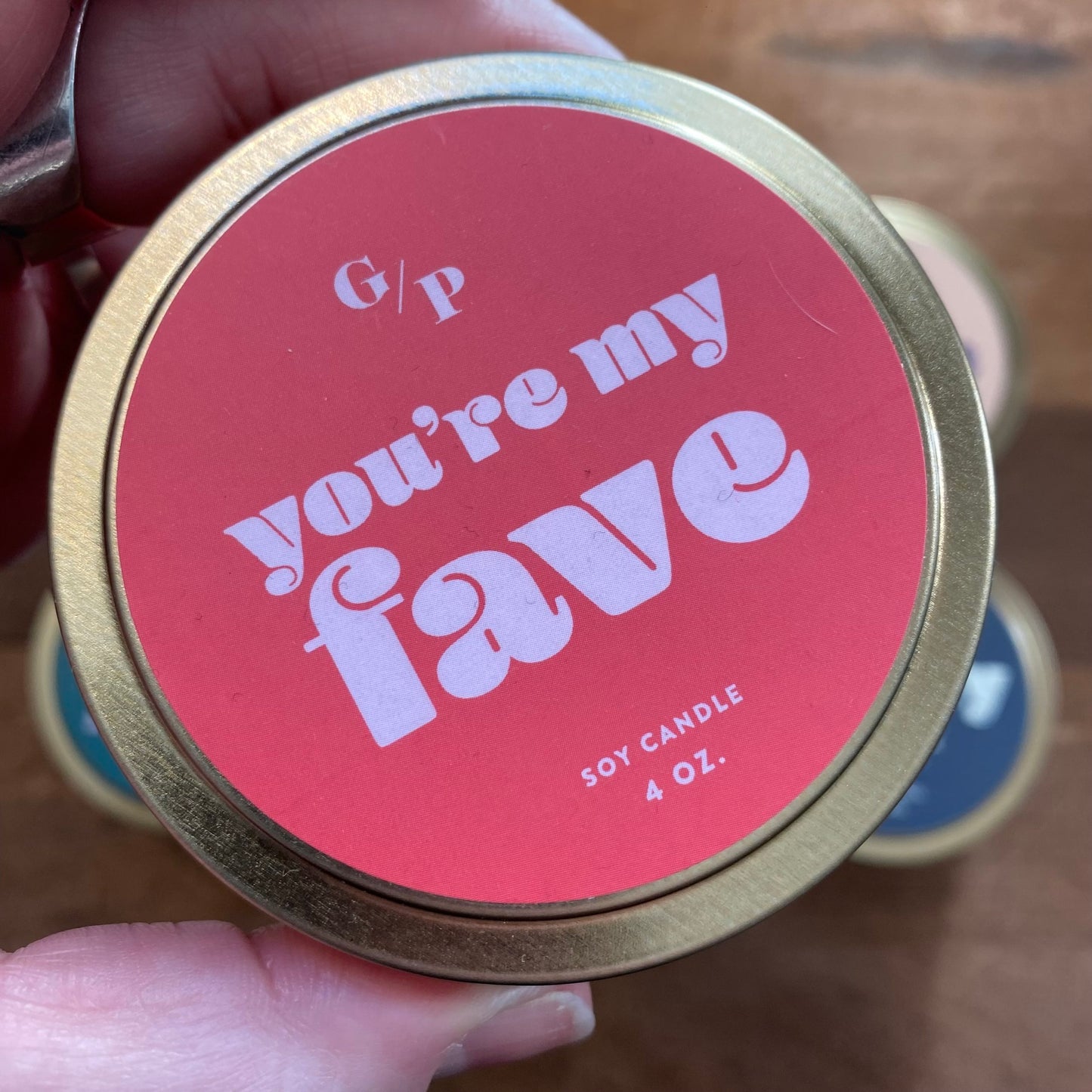 A person holding a 4 oz Tin Collection Soy Candle II from GP Candle Co with the label "you're my fave" in a pink and gold color scheme.