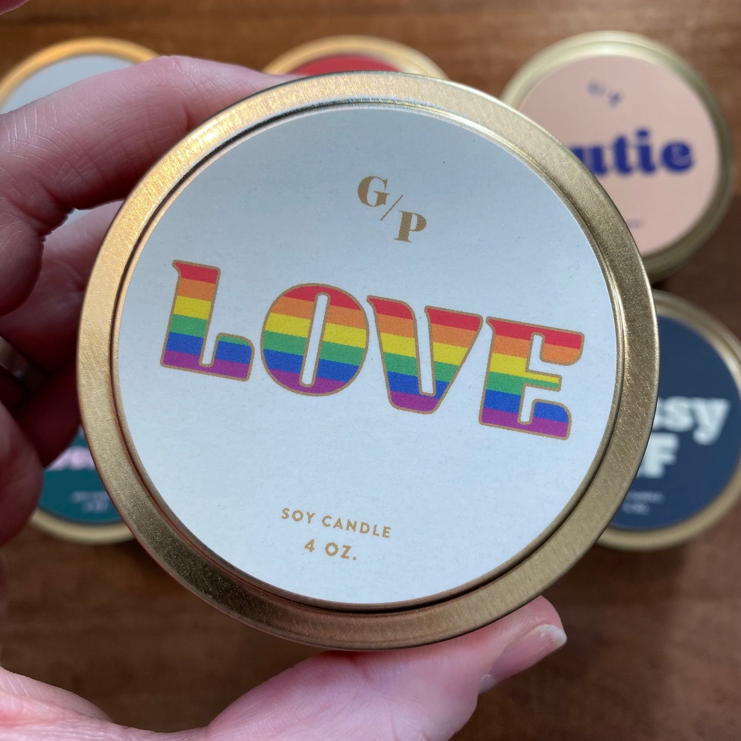 A hand holding a 4 oz Tin Collection Soy Candle II tin with "love" printed on the lid by GP Candle Co.
