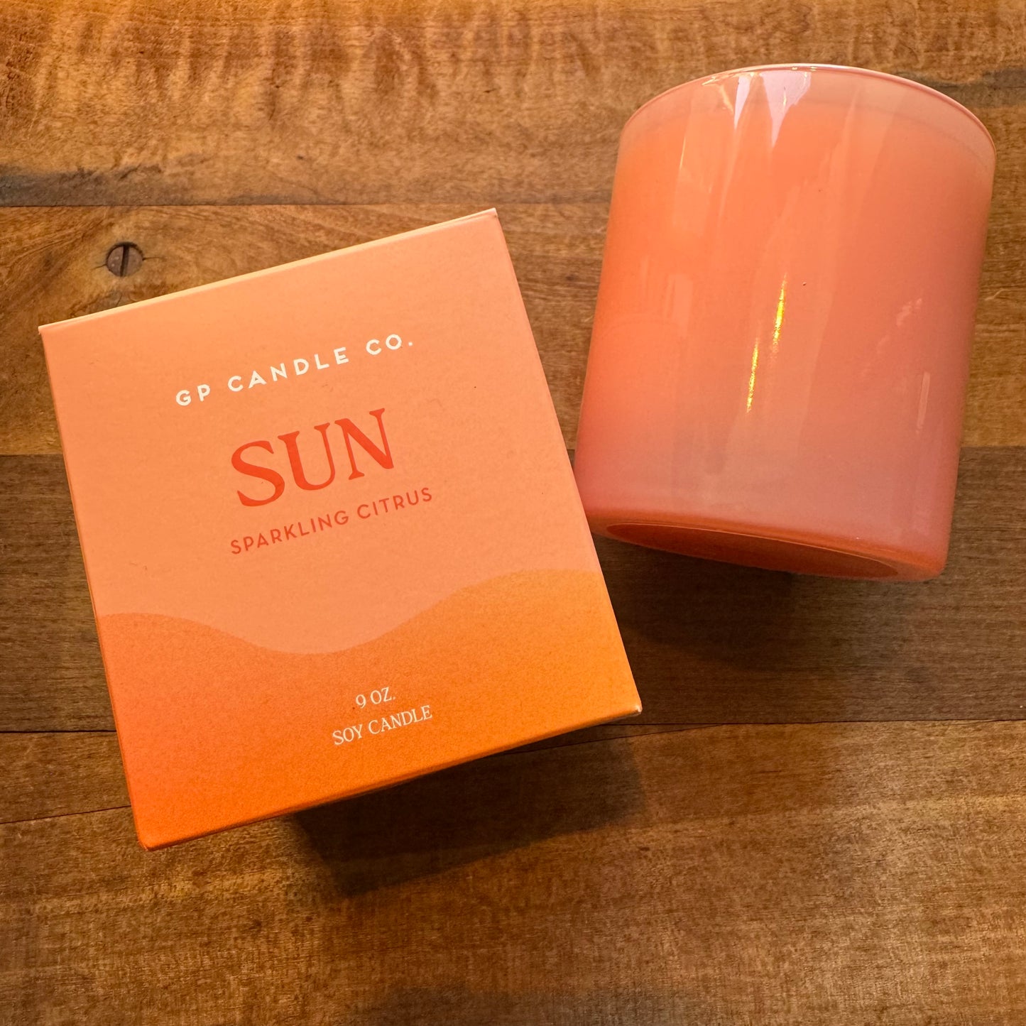 A hand-poured soy candle labeled "sun" from the GP Candle Co Hue Collection with a sparkling citrus scent, alongside its packaging box on a wooden surface.