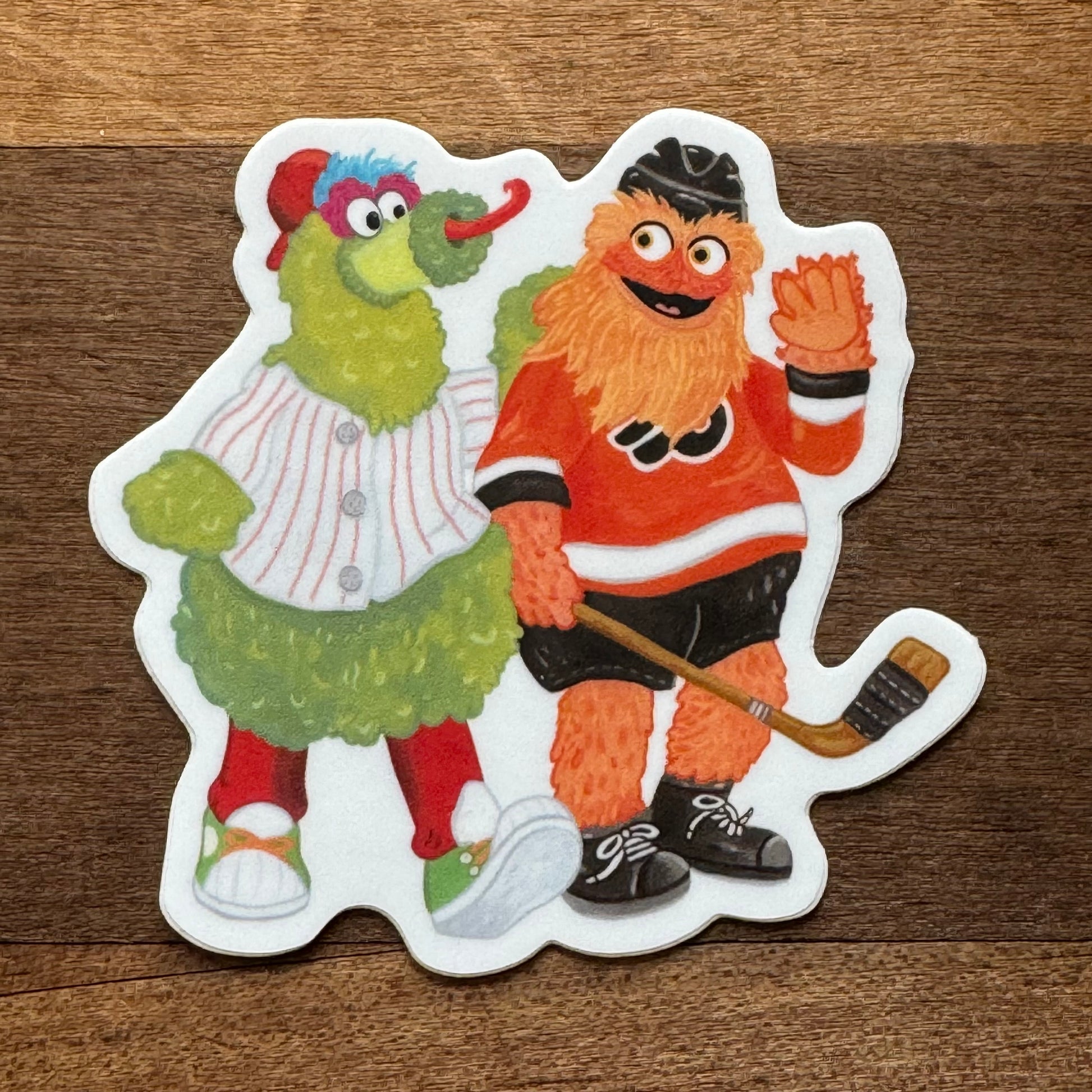 Illustration of two whimsical characters: one dressed as a baseball player and the other as a hockey player, designed as a Gritty & Phanatic BFF sticker by Jamie Bendas.