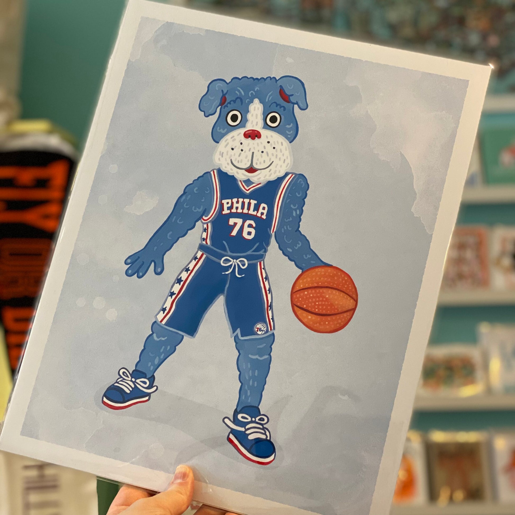 An archival digital print of a cartoon dog dressed in a basketball uniform with the number 76, holding a basketball from Jamie Bendas' Philly Mascot Prints.