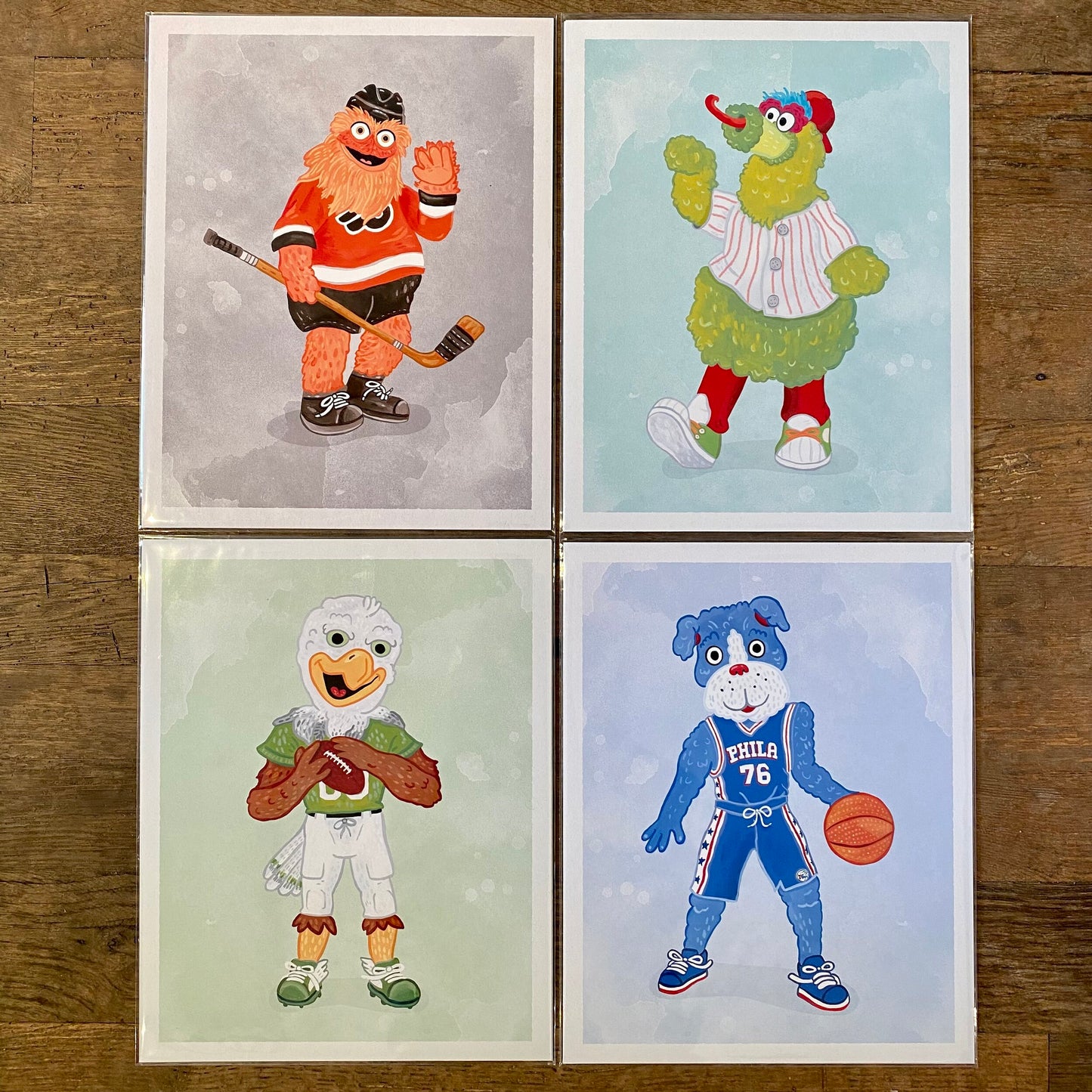 Four illustrations of anthropomorphic animal characters dressed in various sports uniforms representing different teams, transformed into Philly Mascot Prints by Jamie Bendas.