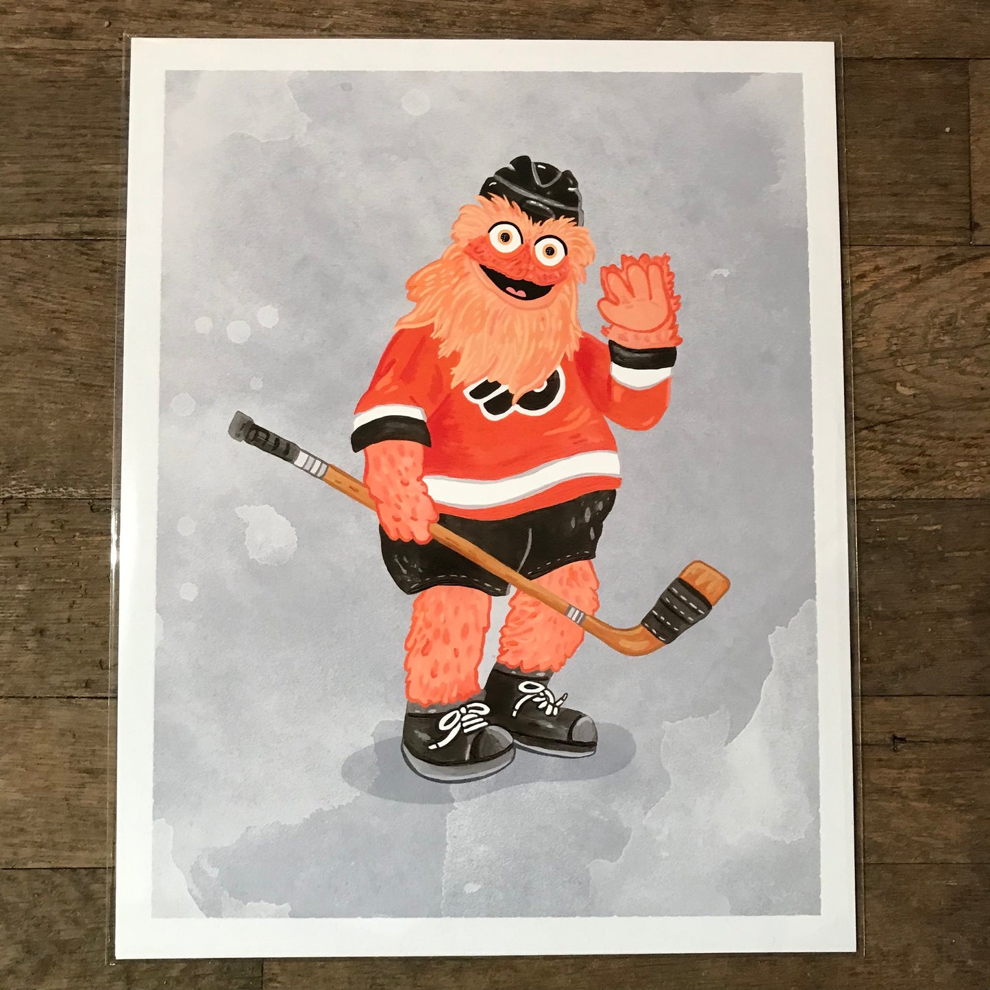 Illustration of a cheerful anthropomorphic orange creature dressed in ice hockey attire, identified as Gritty, waving hello featured on Philly Mascot Prints by Jamie Bendas.