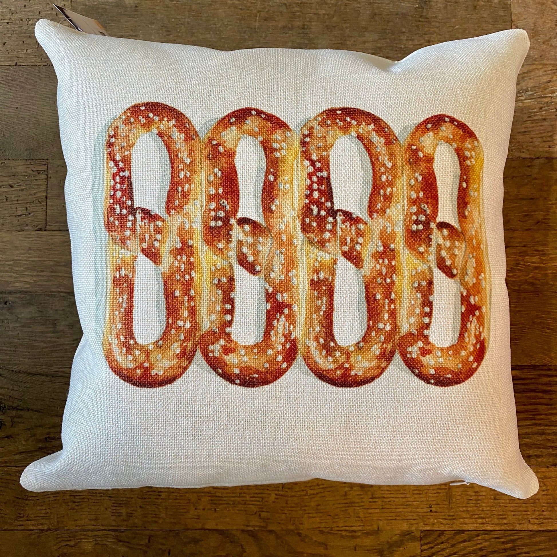 A Philly Illustrated Pillow from Meadowbrook Lane with a printed design of four Philly pretzels on a wooden surface.