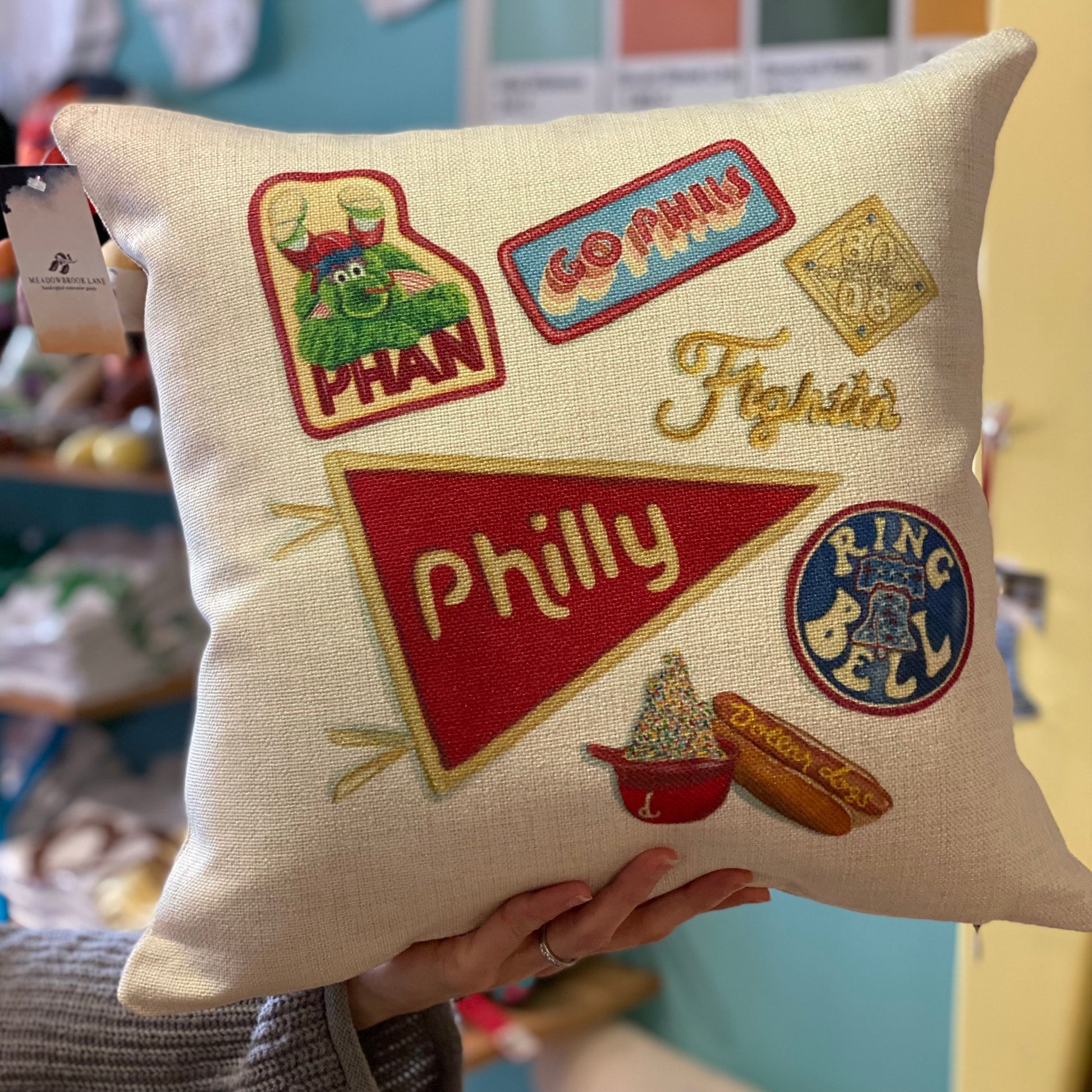 A decorative Philly Illustrated Pillows fan pillow by Meadowbrook Lane with Philly-themed embroidered patches, including the Liberty Bell and a cheesesteak.