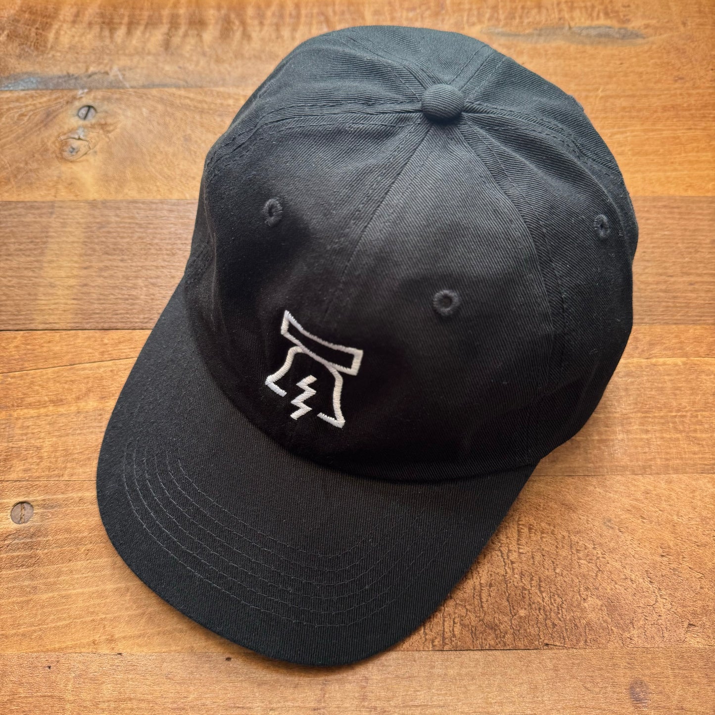 Bell & Bolt baseball cap with a white abstract logo embroidered on the front, displayed on a wooden surface by Philadelphia Independents.