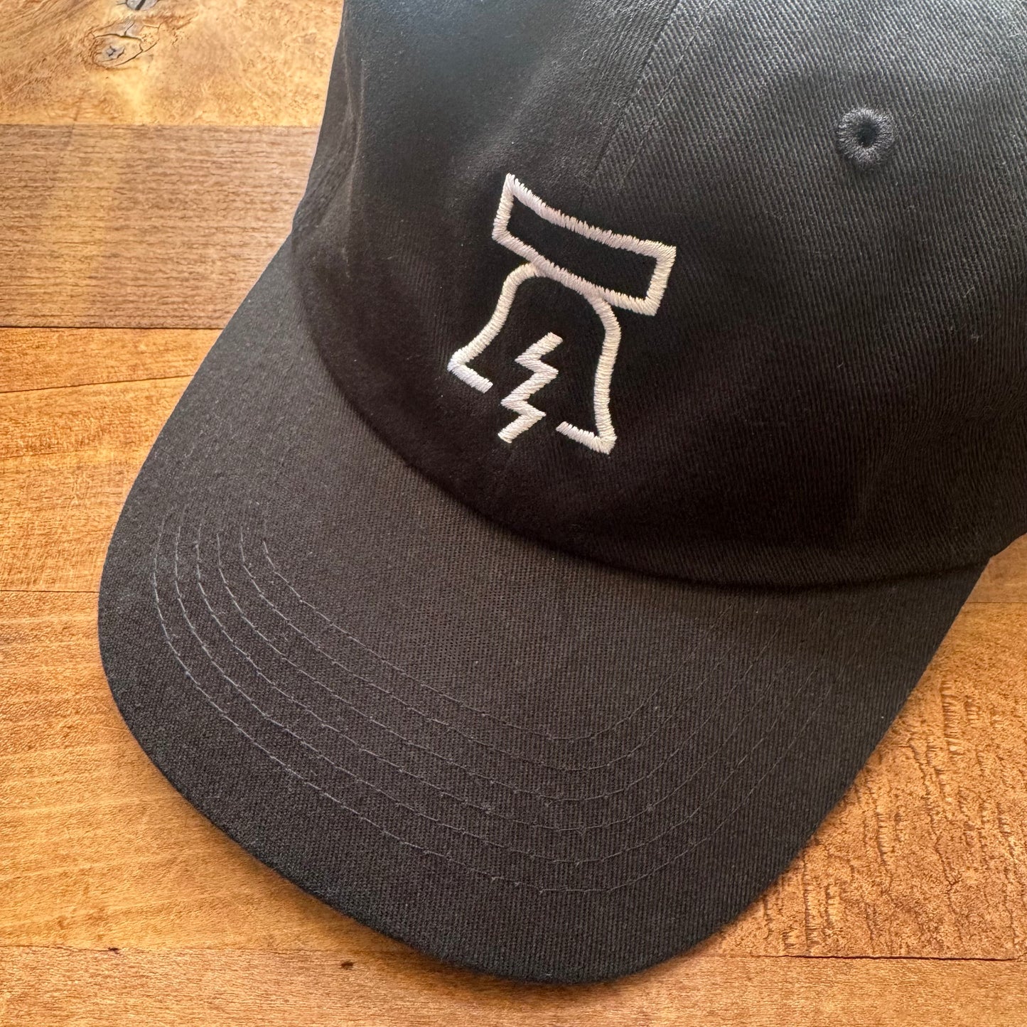 Bell & Bolt Baseball Hat with a white embroidered logo featuring a stylized lightning bolt on a wooden surface by Philadelphia Independents.