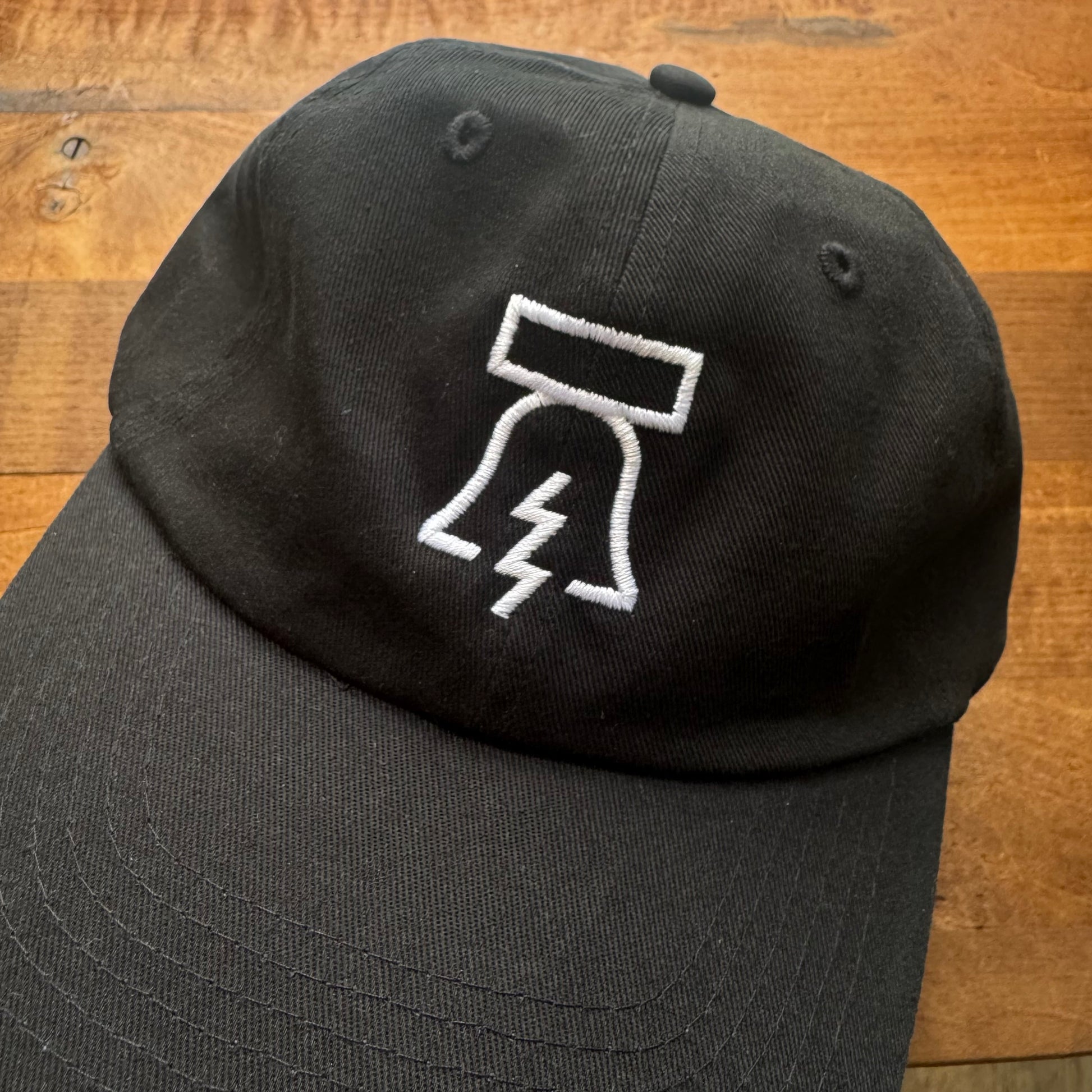 Bell & Bolt Baseball Hat with a white embroidered Philadelphia Independents thunderbolt and rectangle logo on a wooden surface.