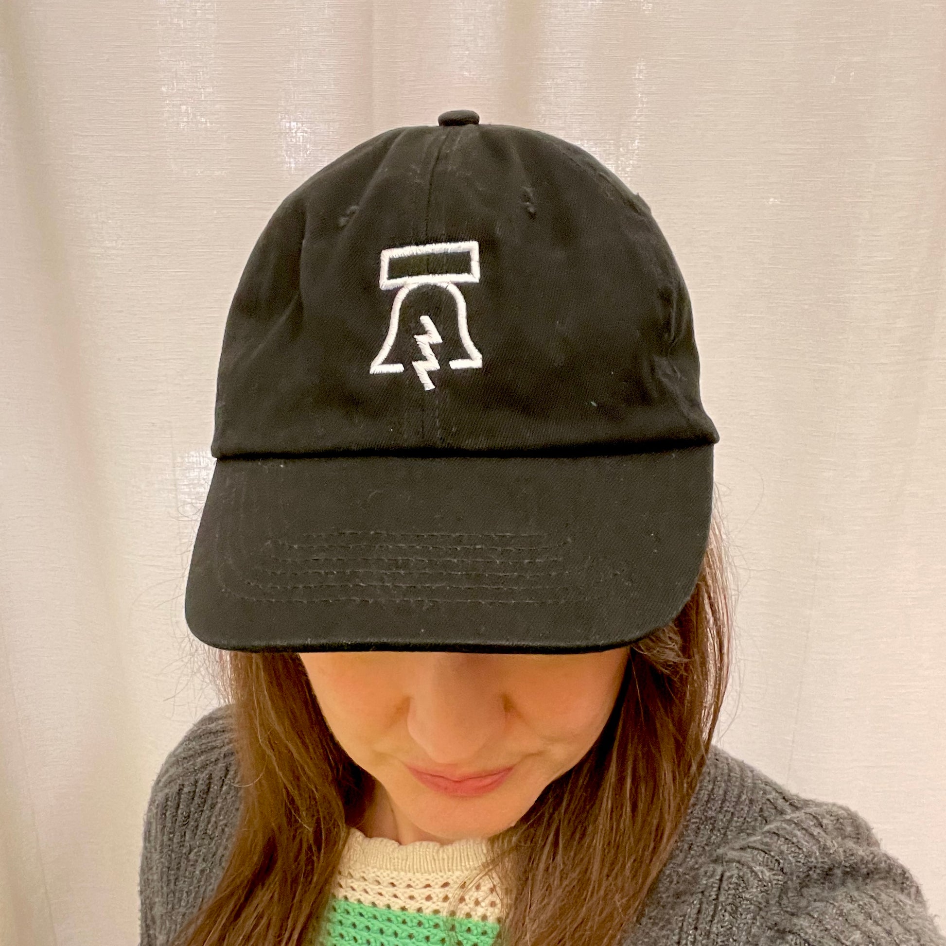 A person wearing a Philadelphia Independents Bell & Bolt Baseball Hat, with a white abstract logo, looking downward with only the top half of their face visible.