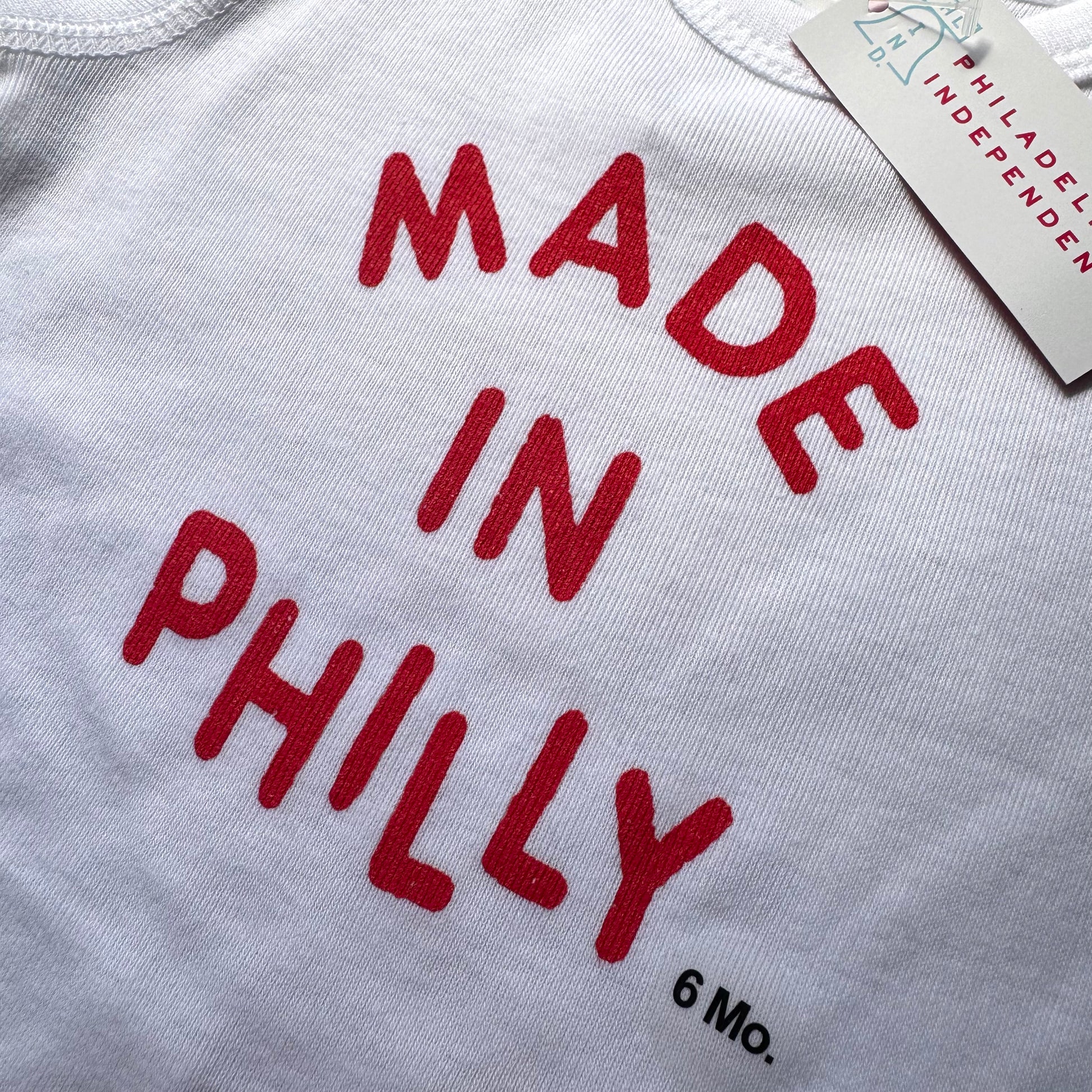 Philadelphia Independents Made in Philly Baby Onesie, featuring a tag indicating 6 months size and crafted from 100% cotton.