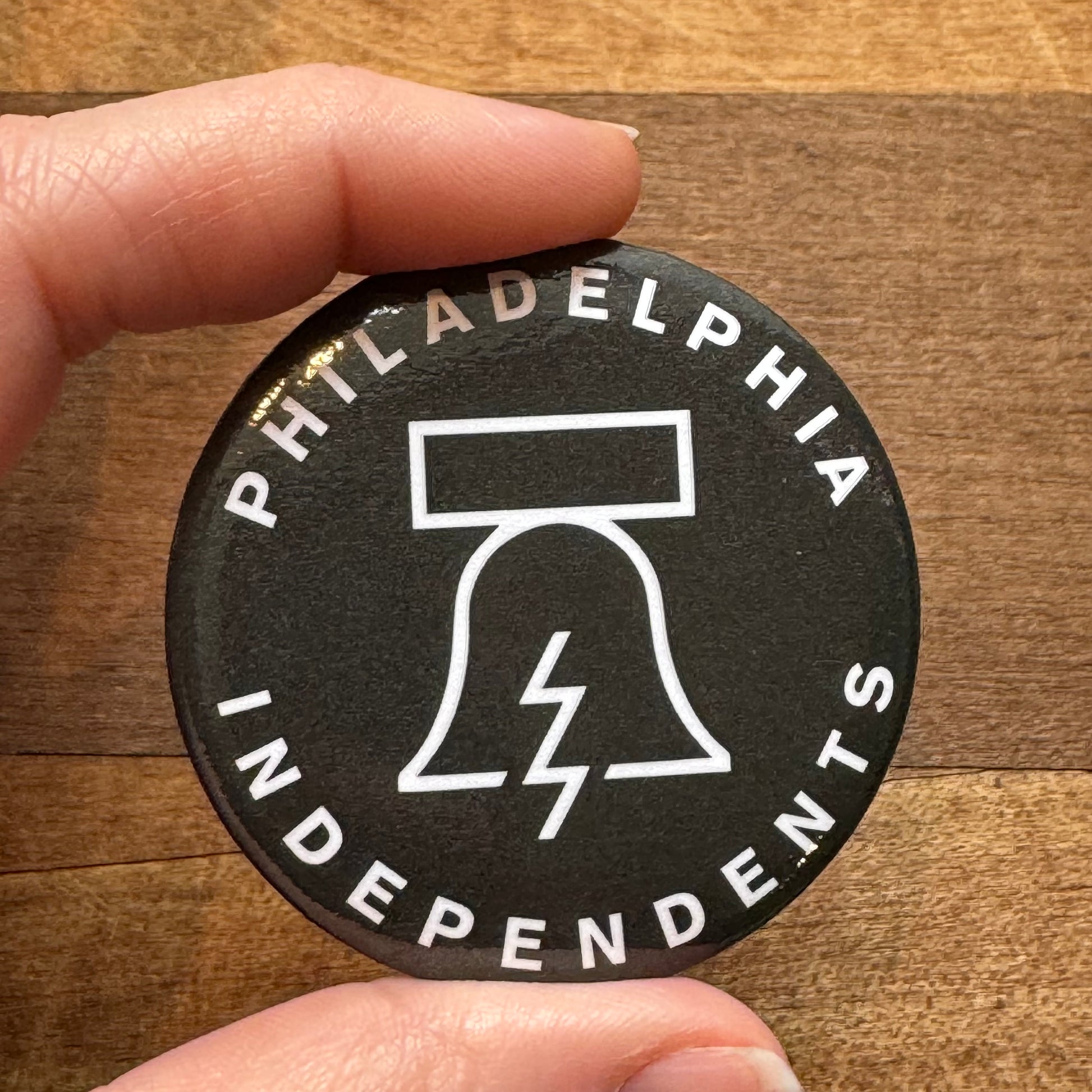 A close-up of a person's hand holding a Bell & Bolt Magnet with the text "Philadelphia Independents" and a graphic of a liberty bell merged with a lightning bolt.