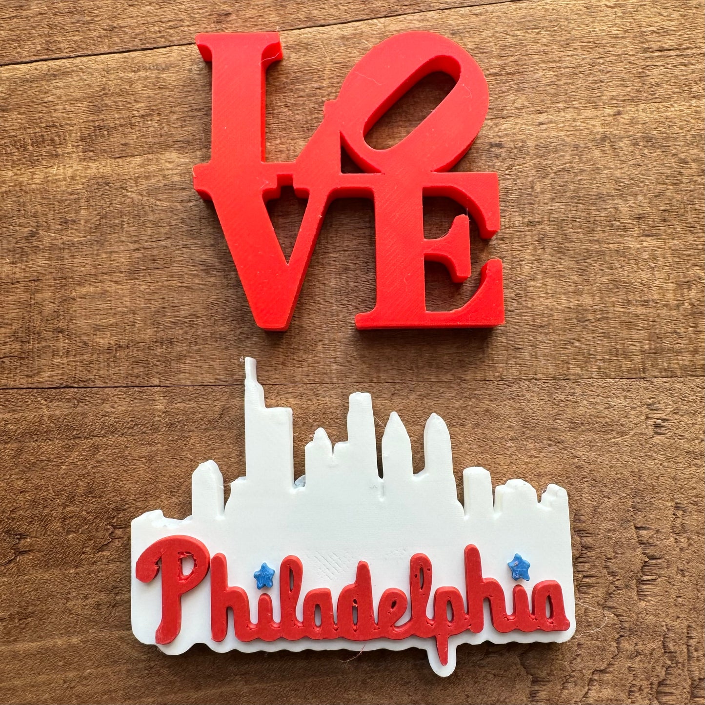 Red "love" sculpture above a white "Philadelphia Skyline" silhouette, both placed against a wooden background. - Philly Magnets by Rosewood Home