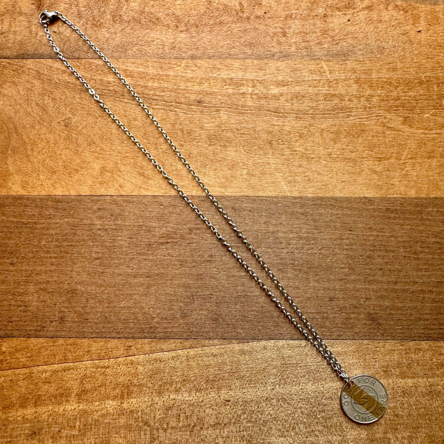 An INDICAN Septa Token Necklace, featuring a circular SEPTA token pendant, lays flat on a wooden surface, showcasing true Philly pride.