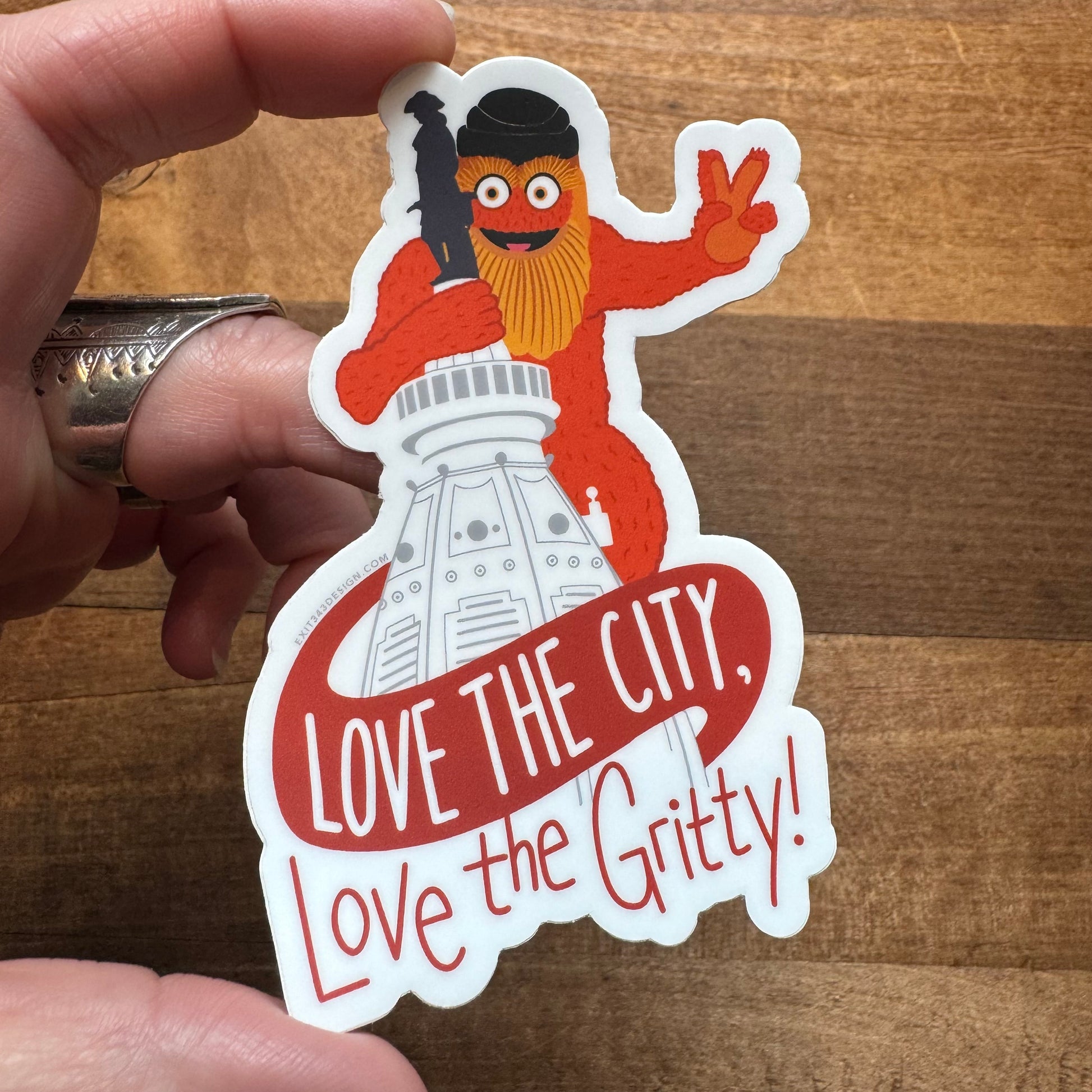 A hand holding a Philly Stickers featuring the mascot Gritty with the phrase "Love the city, love the Gritty," made by exit343design.